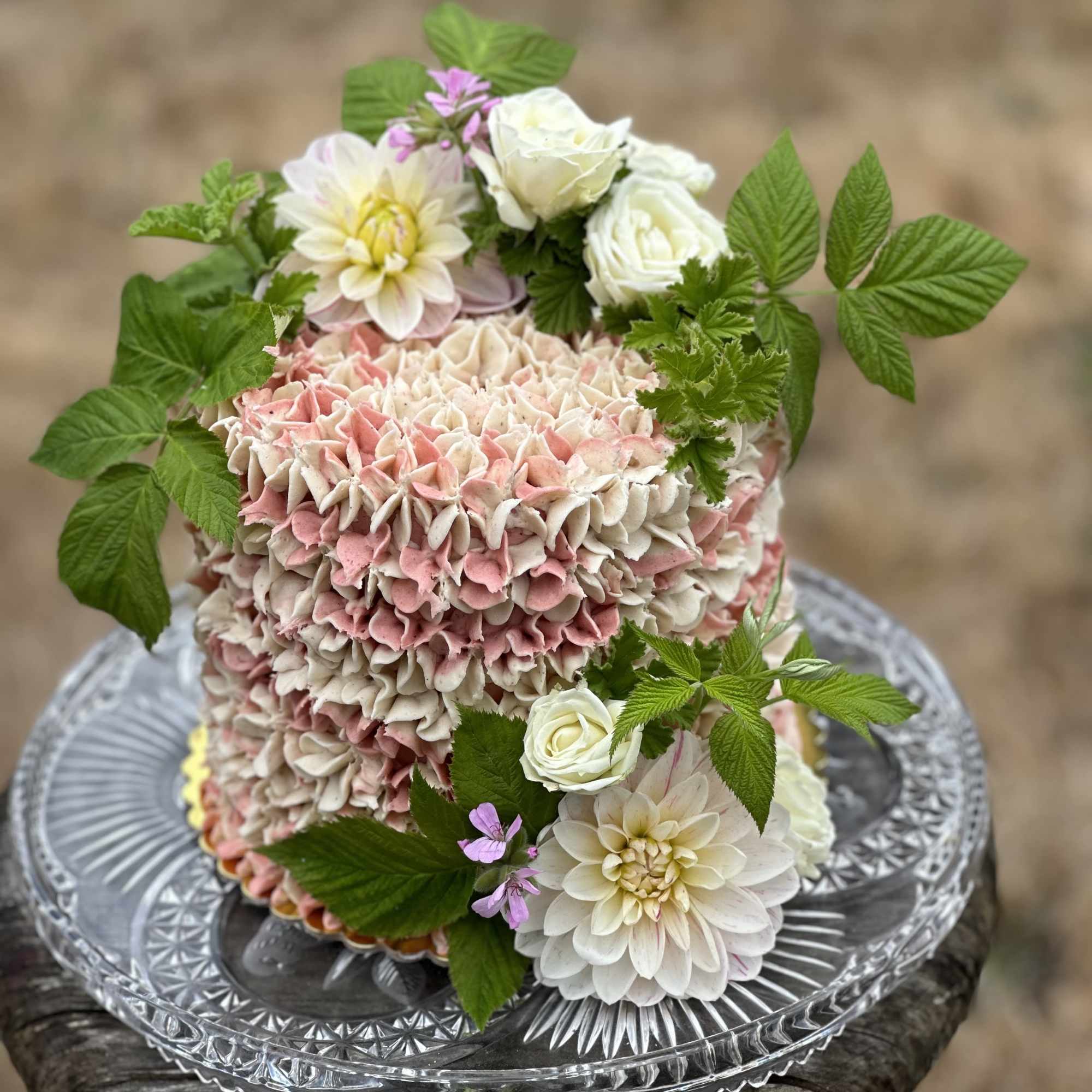 Pink and white floral cake with roses and dahlias on a glass stand