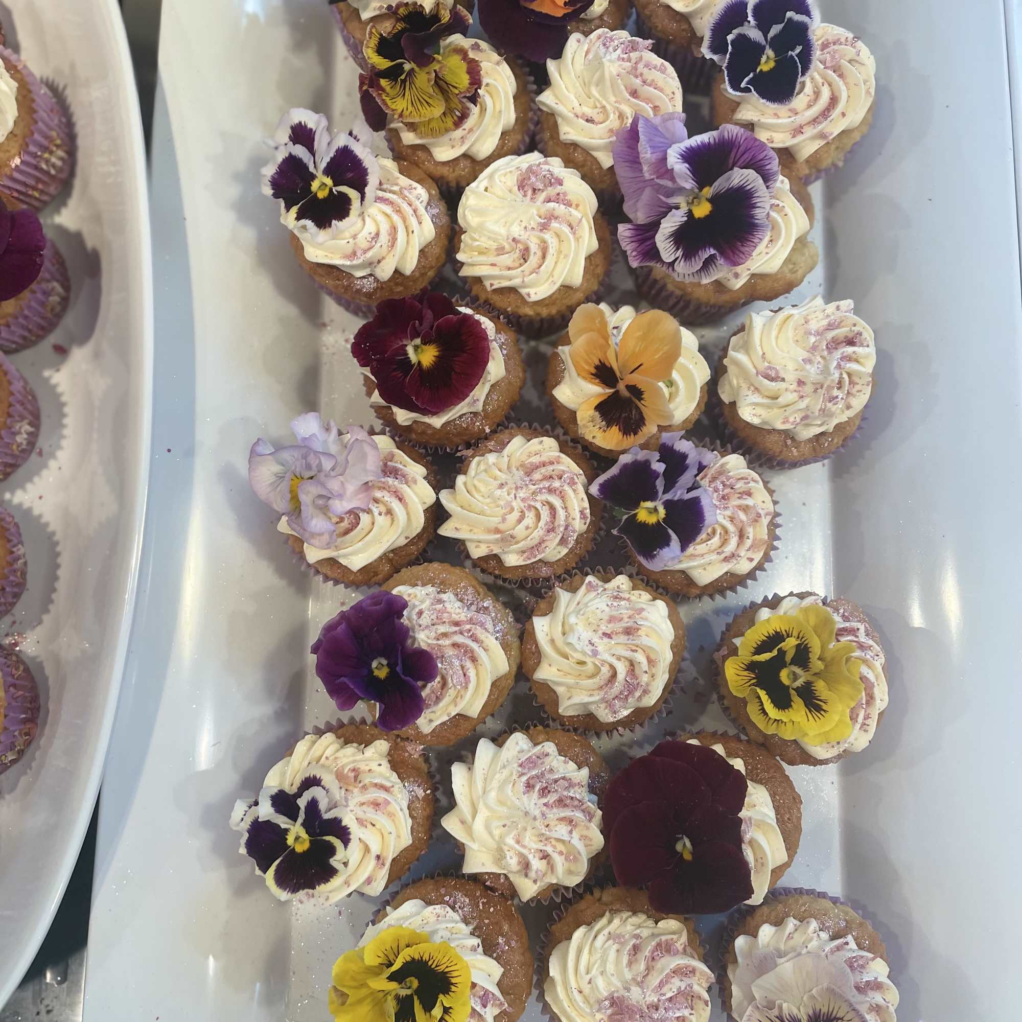 Tray of frosted cupcakes topped with colorful edible flowers