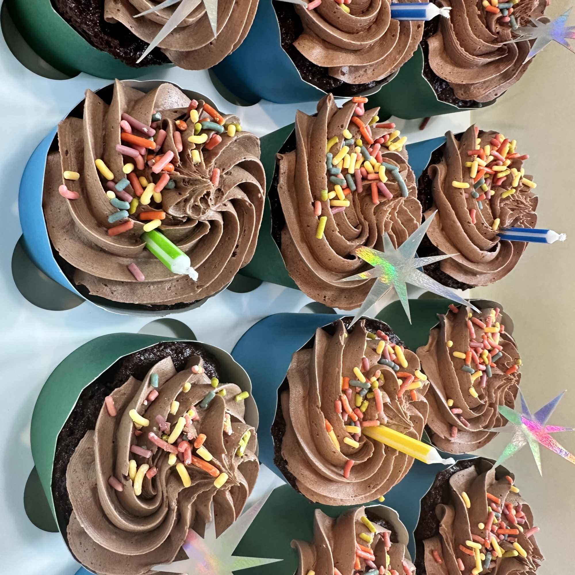 Cupcakes with chocolate frosting and rainbow sprinkles in teal wrappers