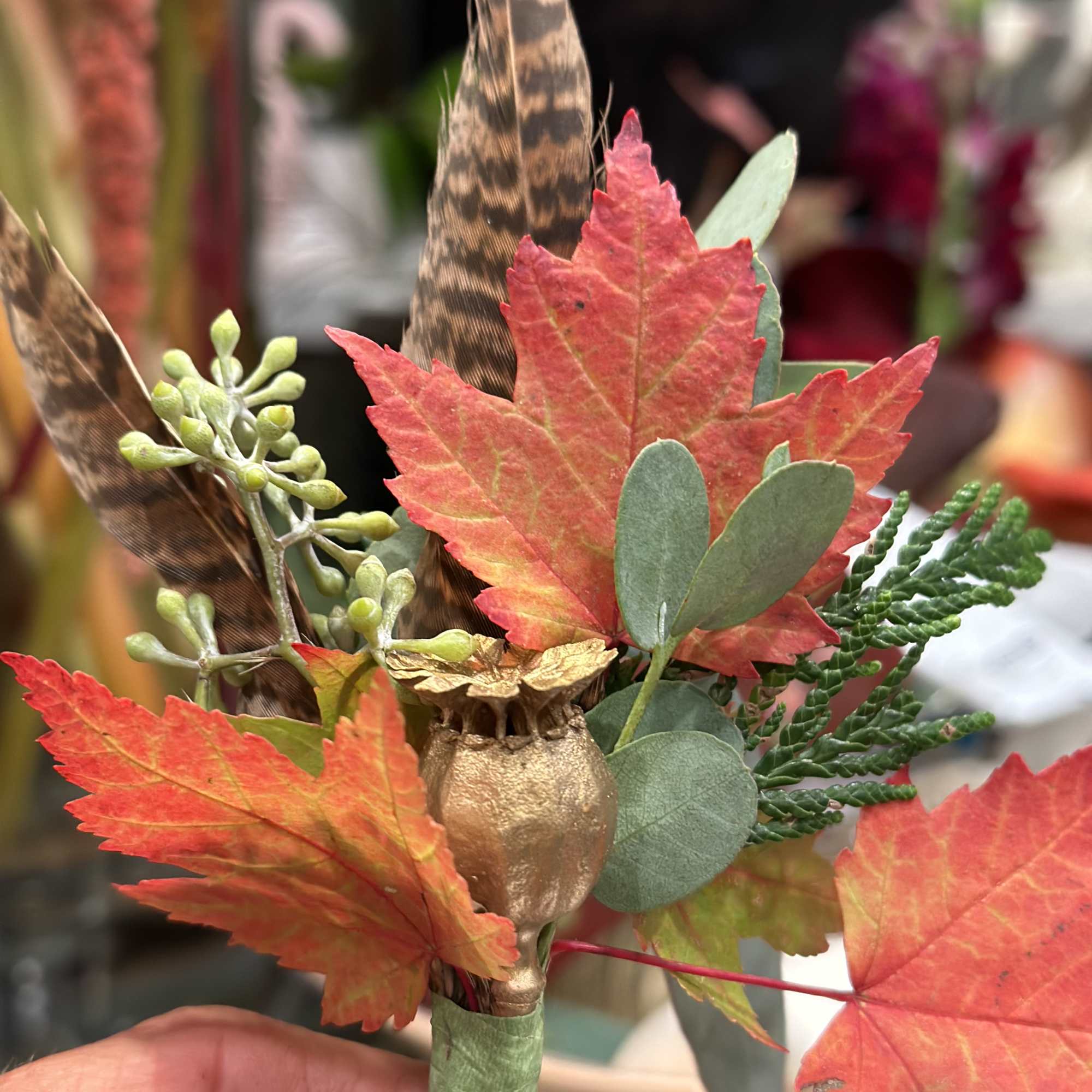 Small boutonniere with red leaves, feathers, and a gold acorn accent