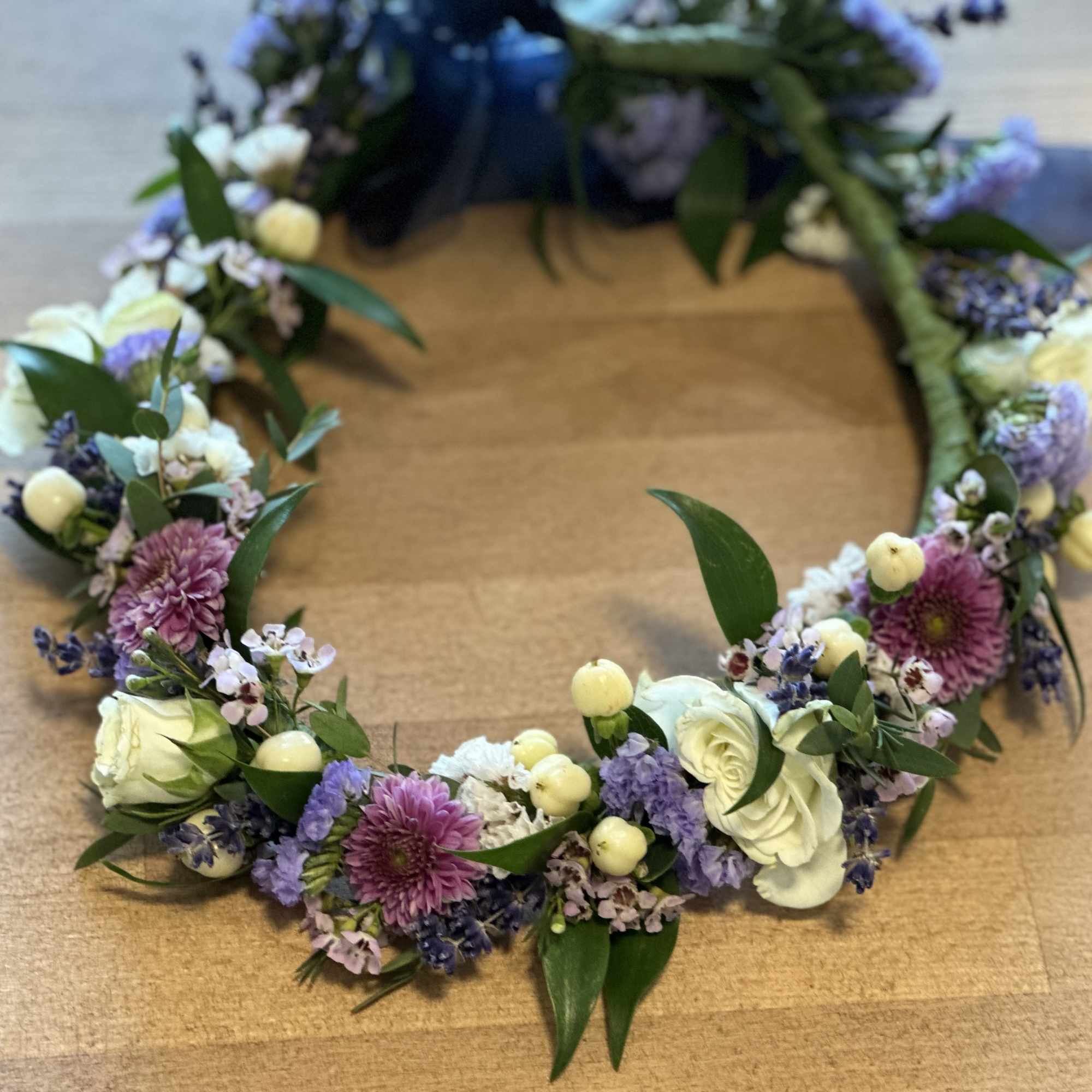 Floral wreath with white, purple, and pink blooms on a wooden surface