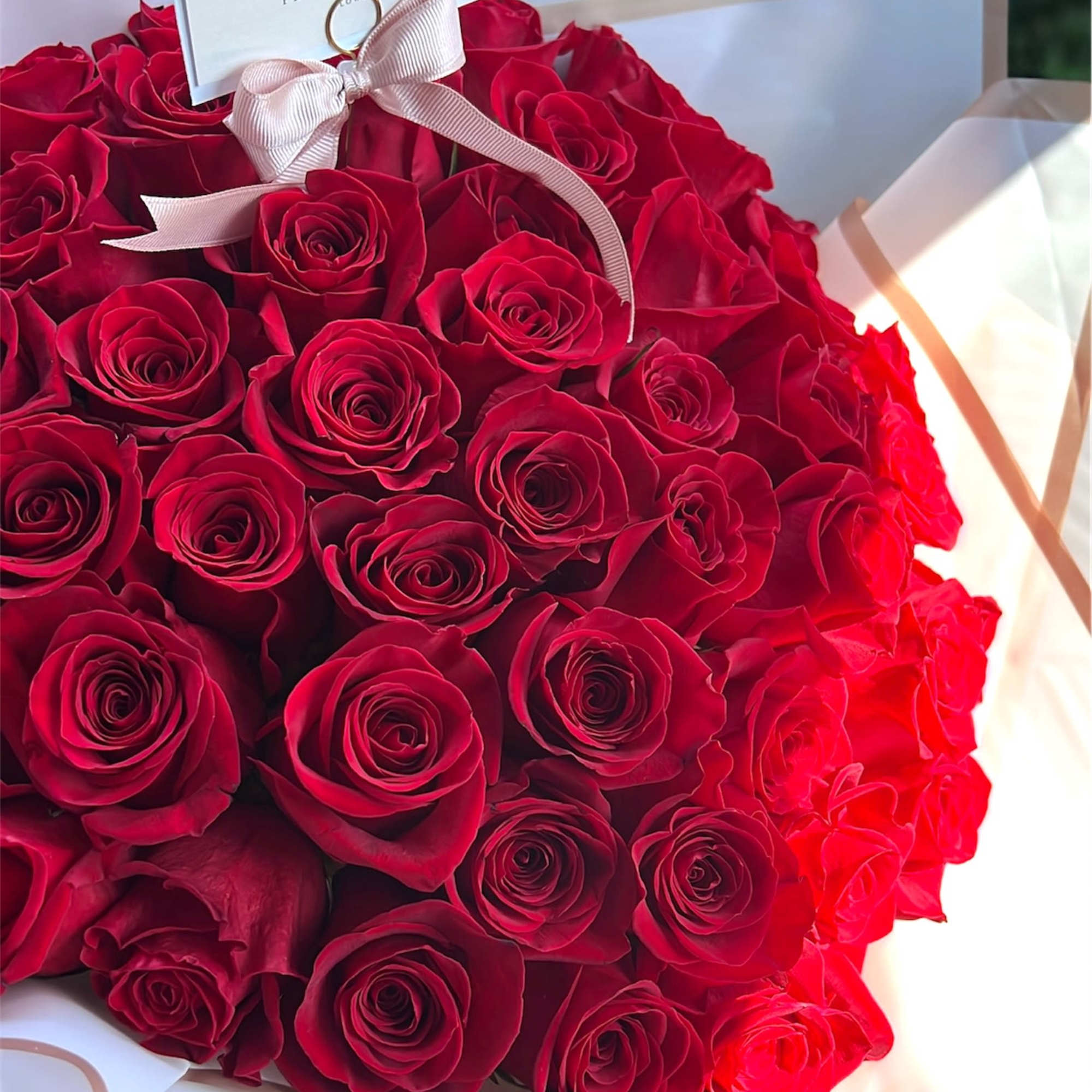 Bouquet of red roses wrapped in white paper with a ribbon and card