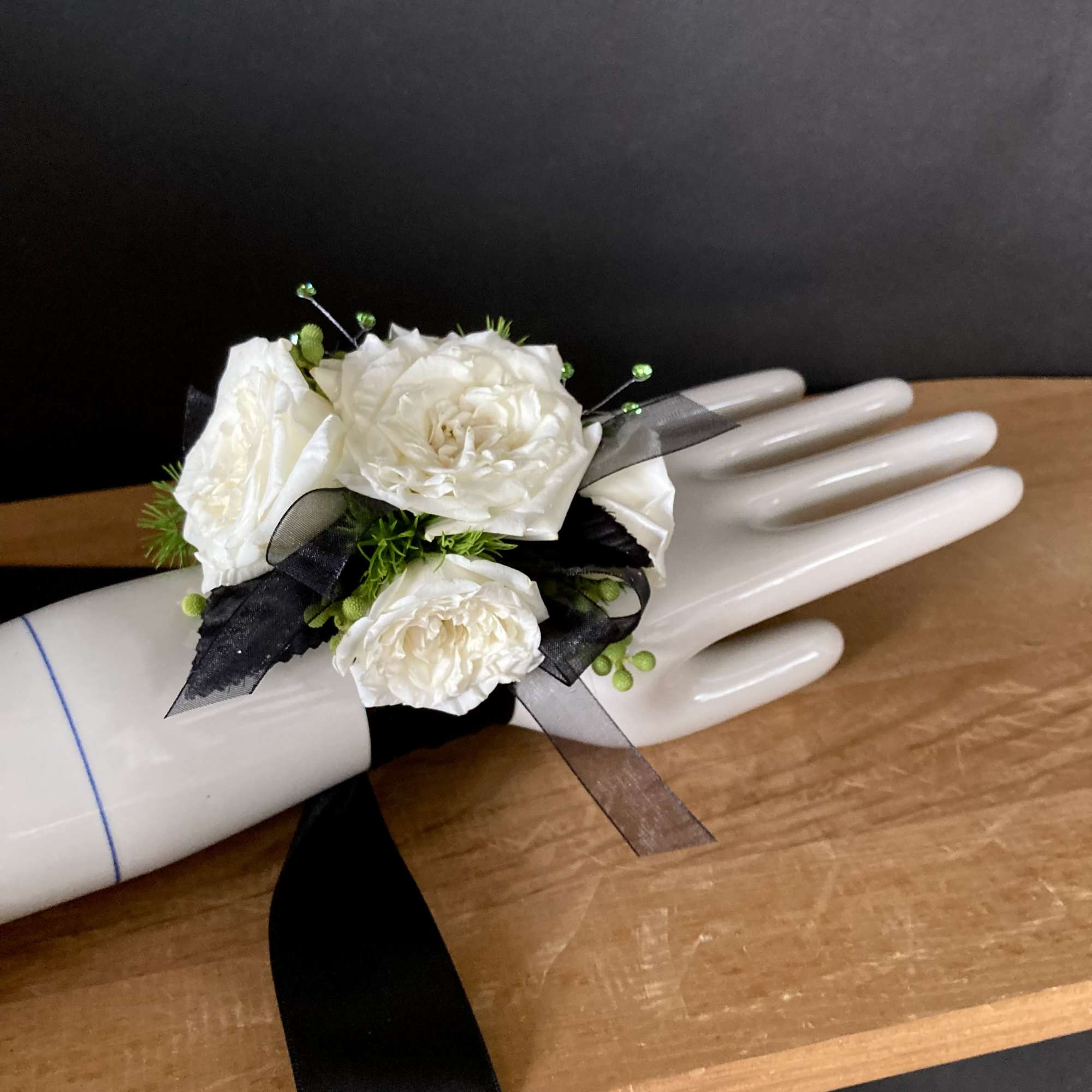 White rose corsage with black ribbon on a mannequin hand