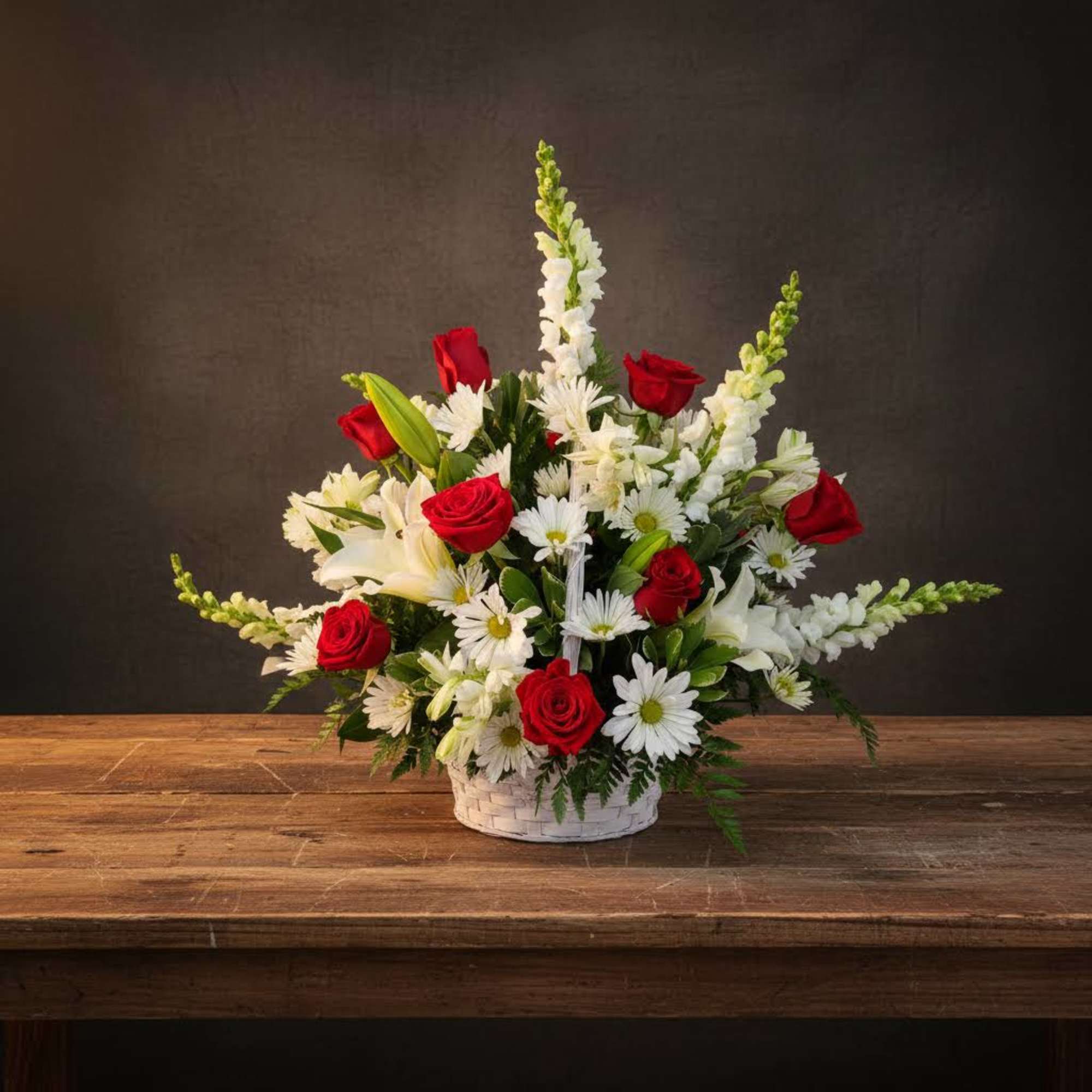 Basket arrangement of red roses, white lilies, and white daisies
