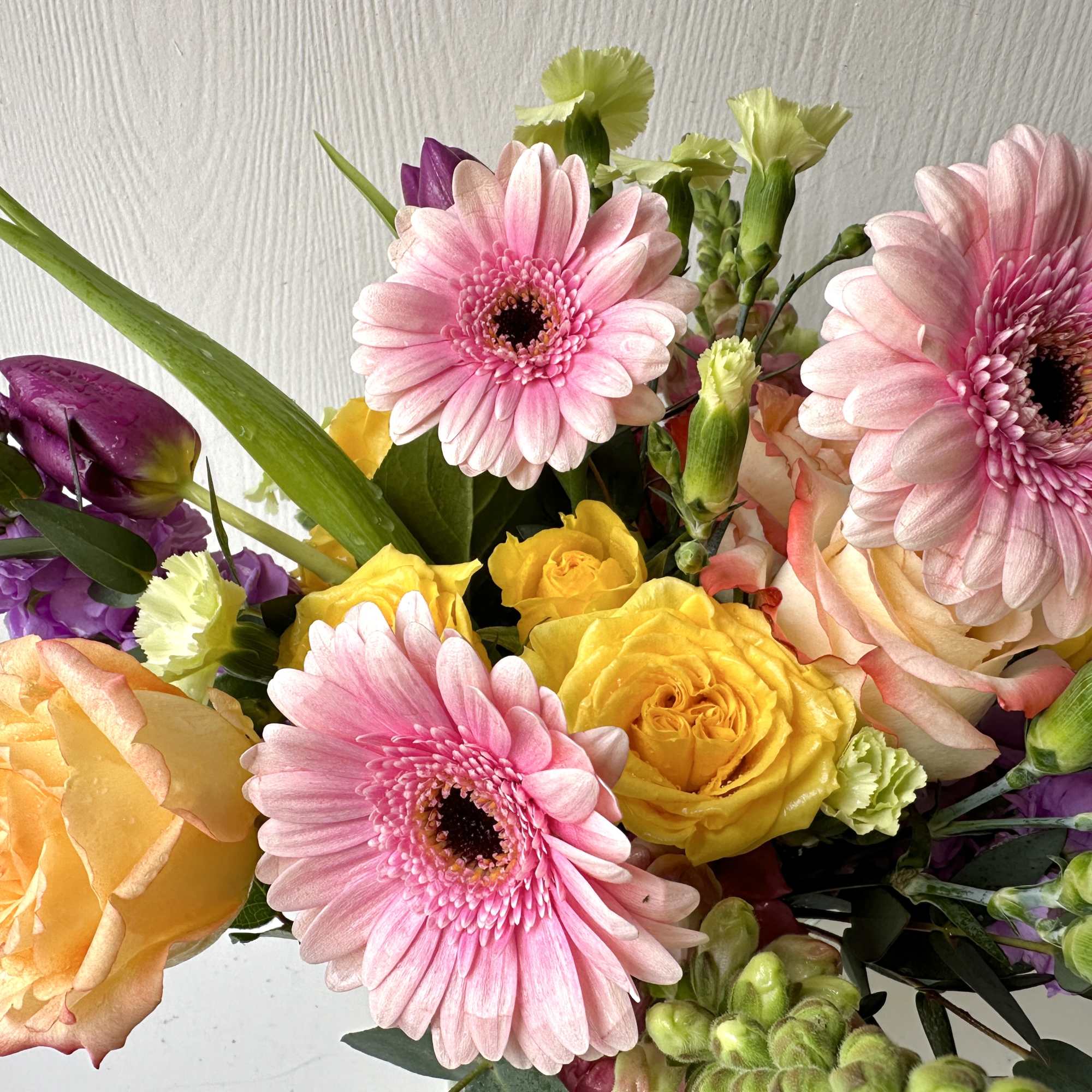 Bouquet of pink gerbera daisies, yellow roses, and purple blooms