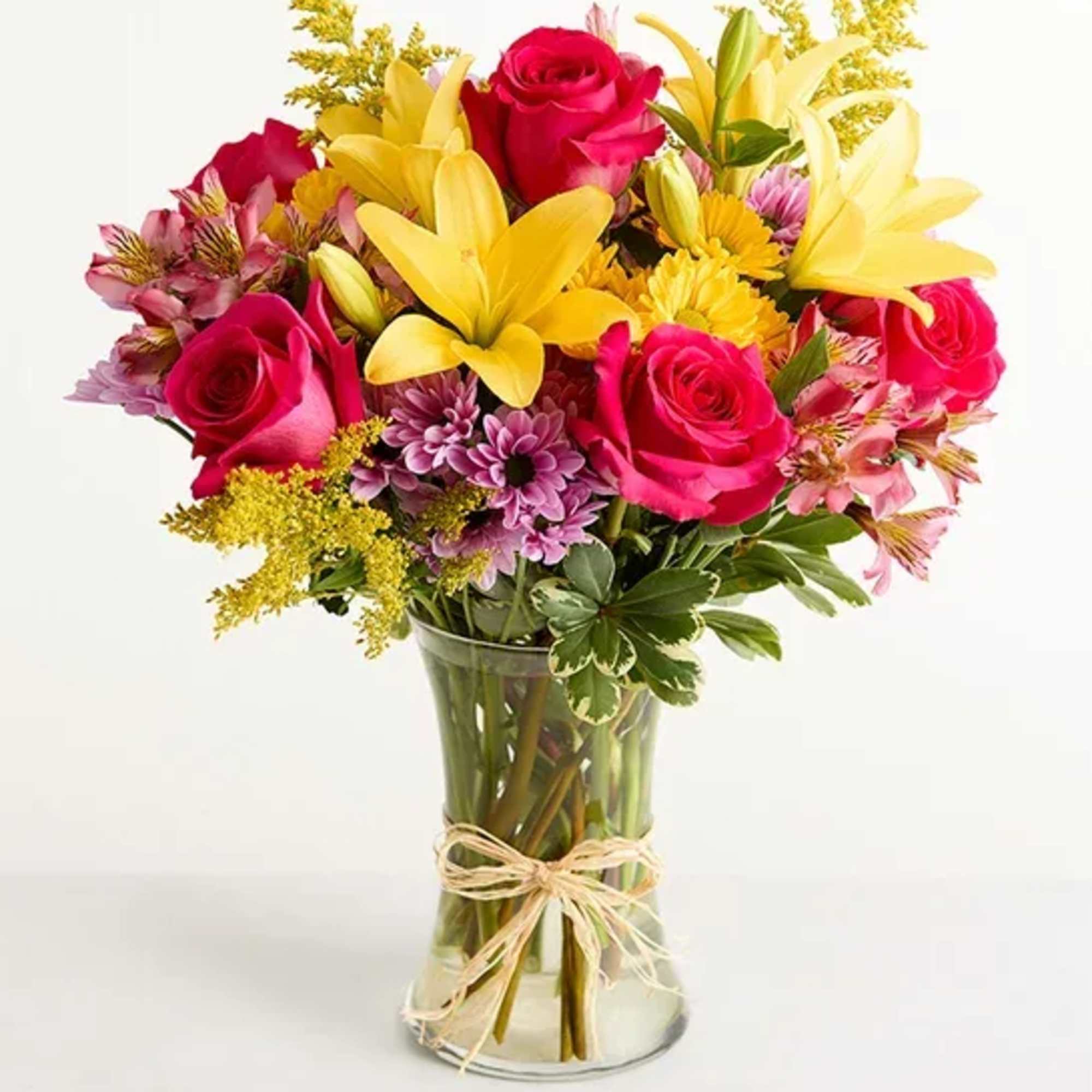 In a clear vase with yellow lilies, hot pink roses, lavender daisies