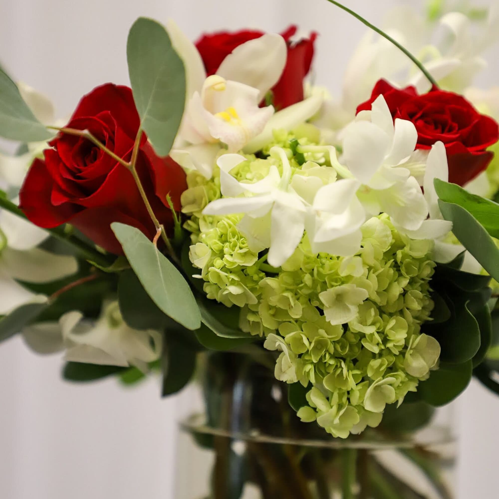 Red roses and white orchids with green hydrangea in a glass vase