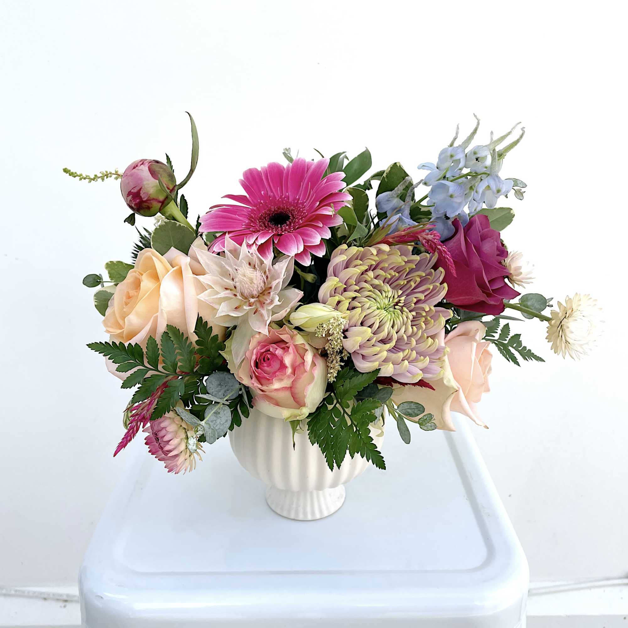 Mixed bouquet in a white vase with pink, peach, and blue flowers
