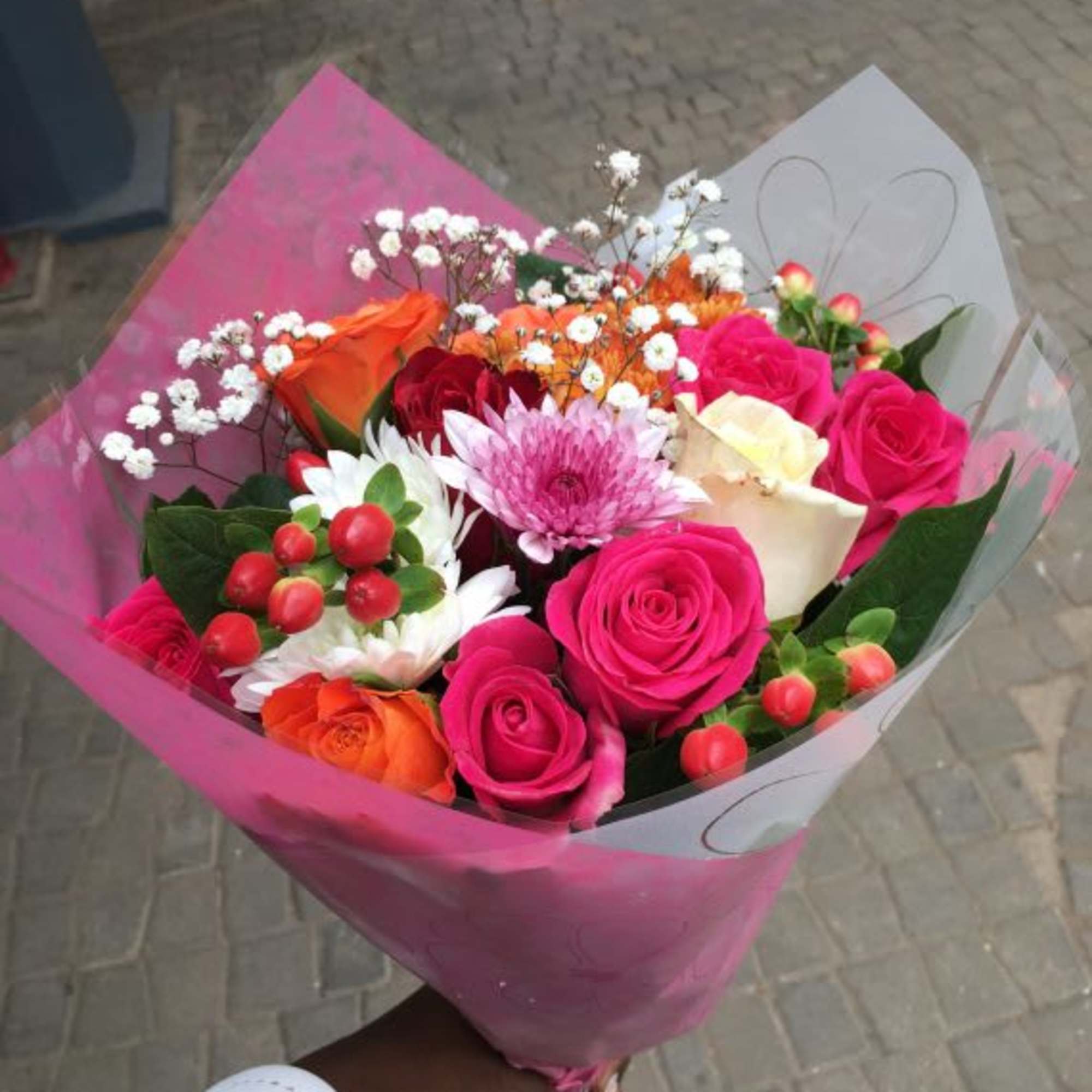Hand-tied bouquet of bright pink and orange roses with white and pink blooms in pink wrapping