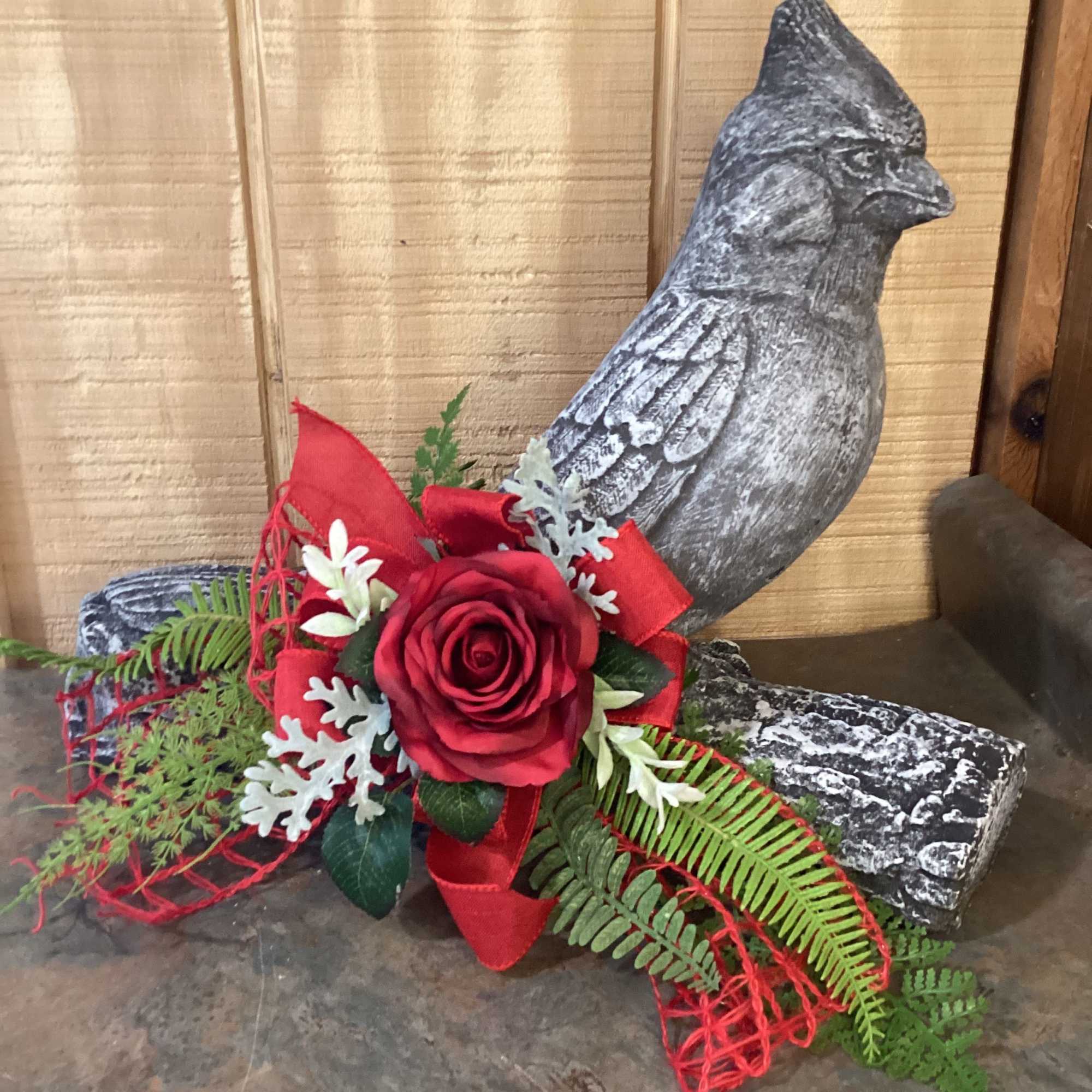 Red rose arrangement with ribbon and fern accents beside a decorative bird statue