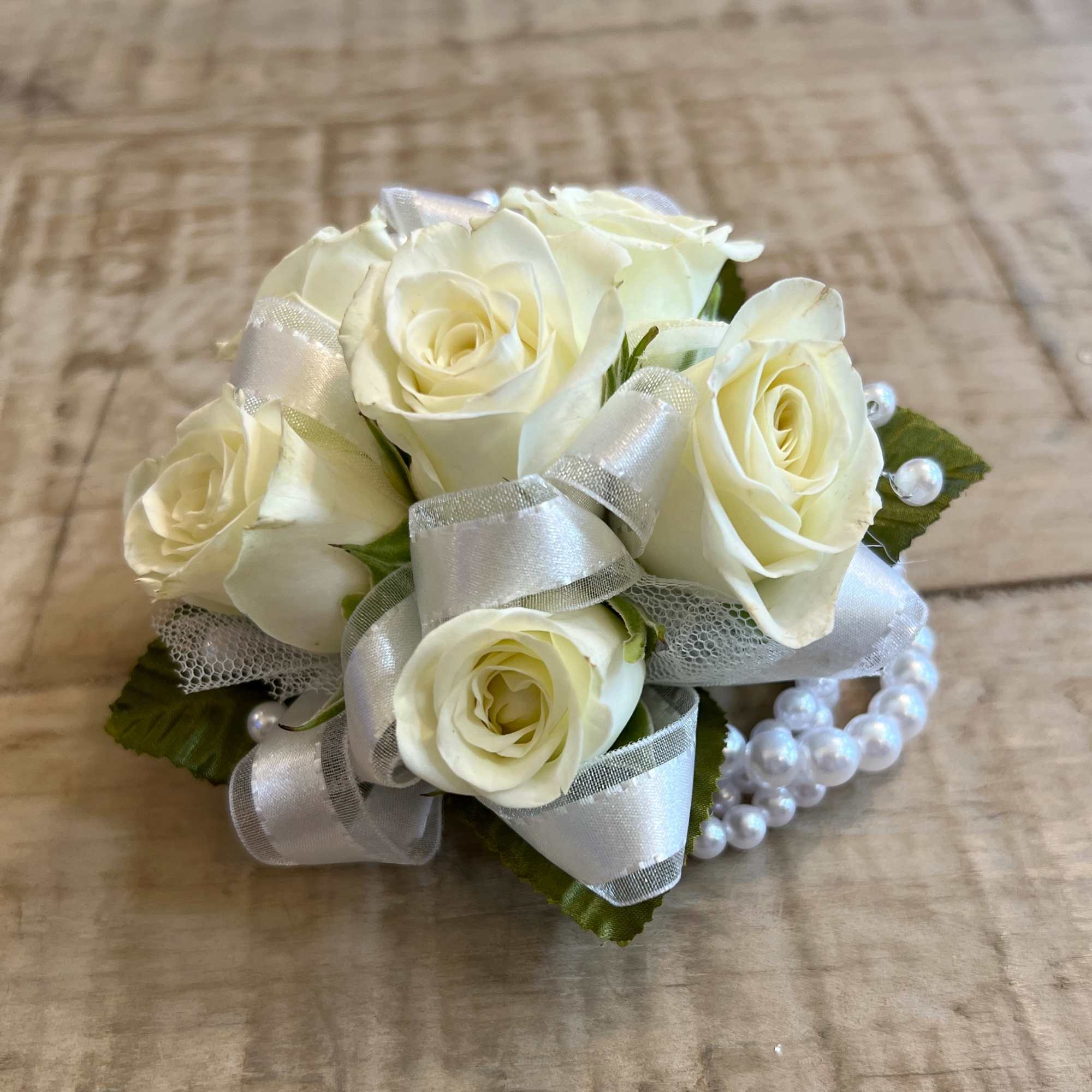 Wrist corsage of ivory spray roses with silver ribbon and a pearl bracelet band