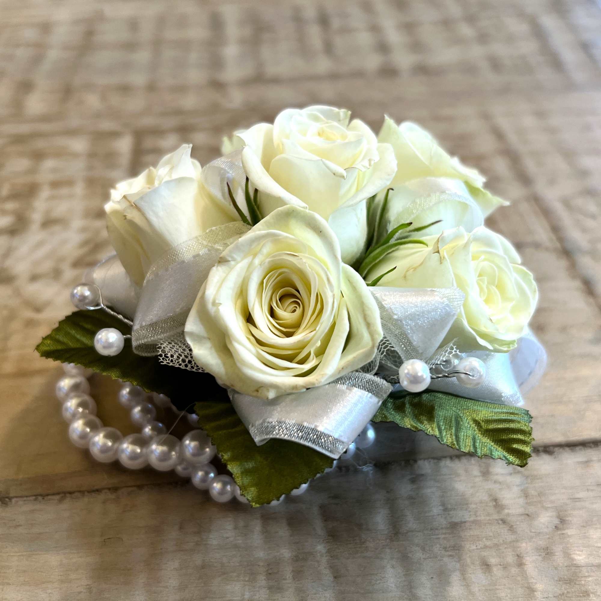 White rose wrist corsage with silver ribbon and pearl bracelet on a wooden surface