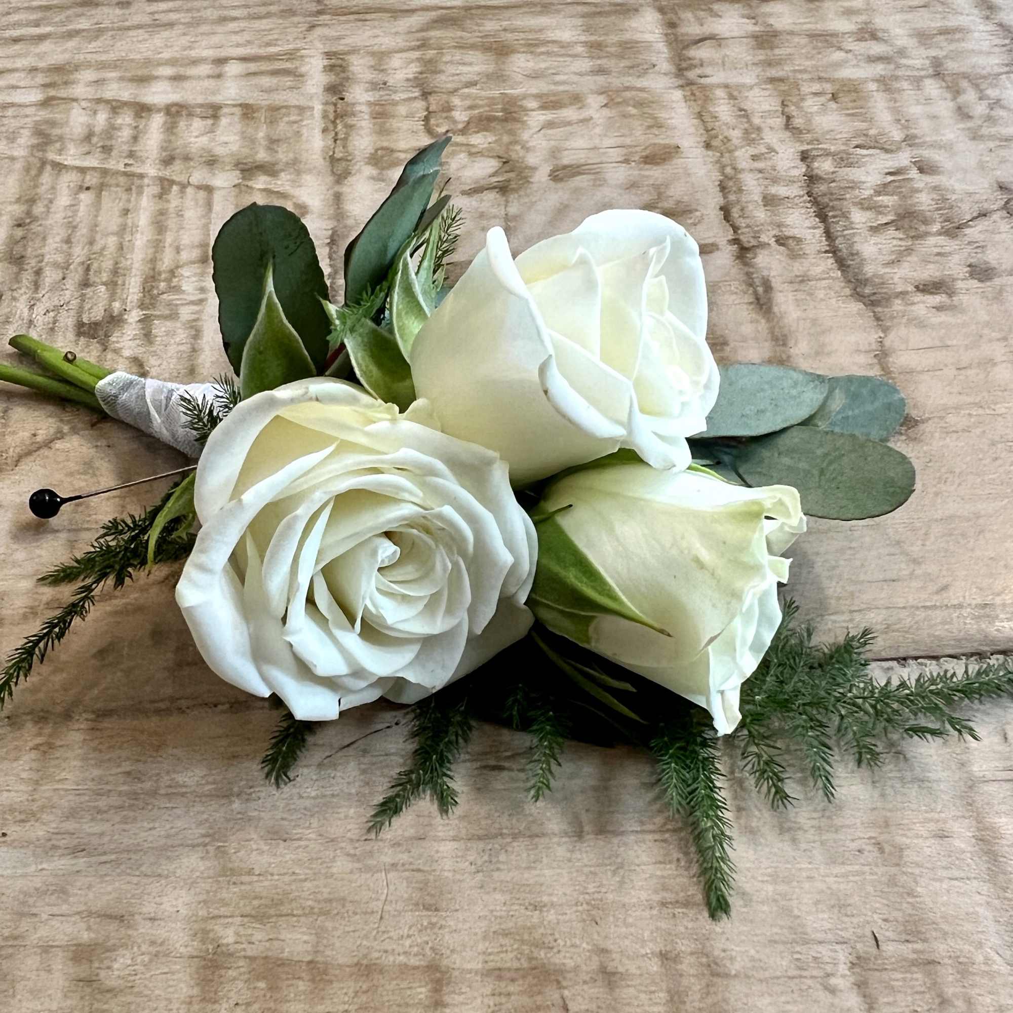 Small bouquet of white roses with greenery on a wooden surface