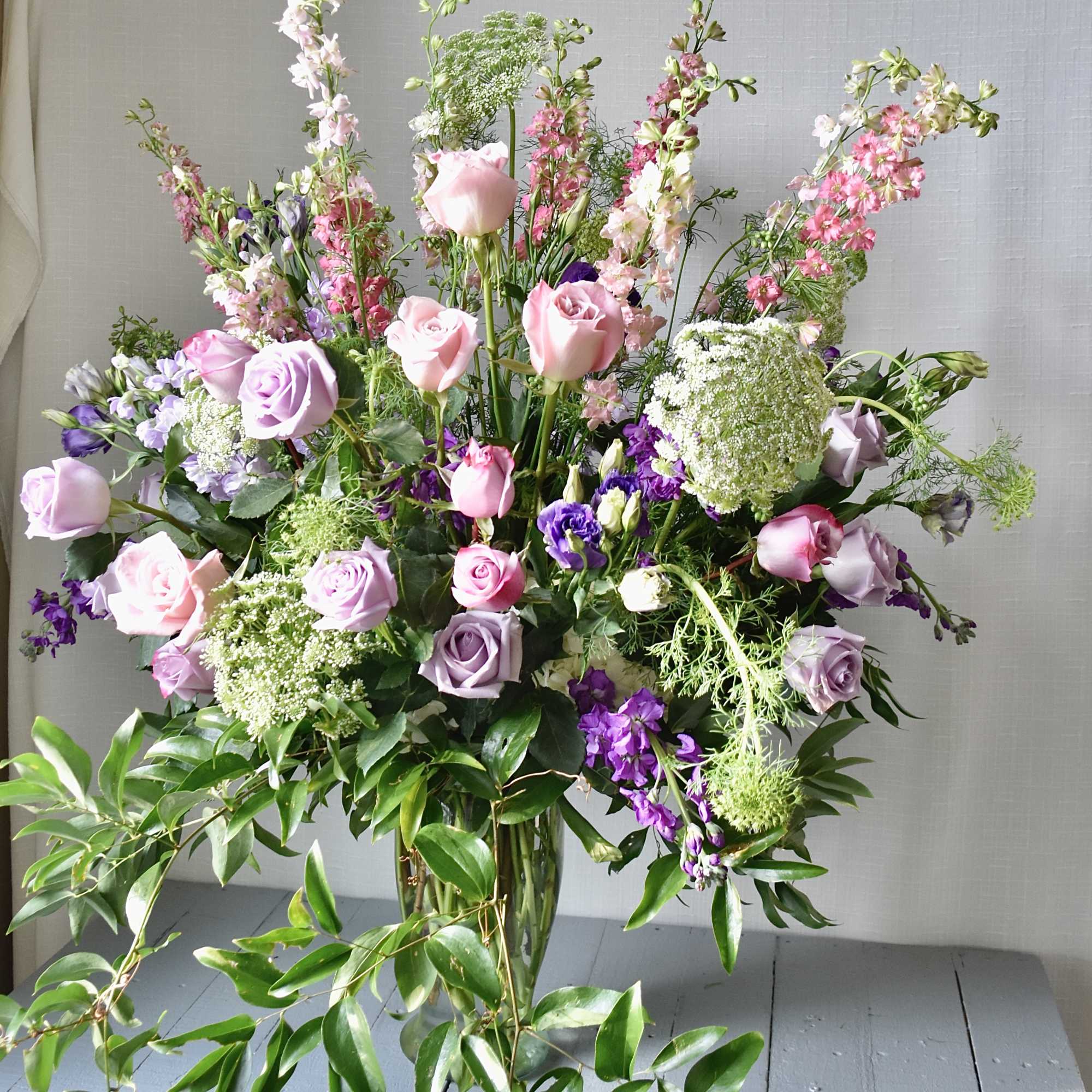 Tall bouquet of pink and lavender roses with purple and white filler flowers in a glass vase