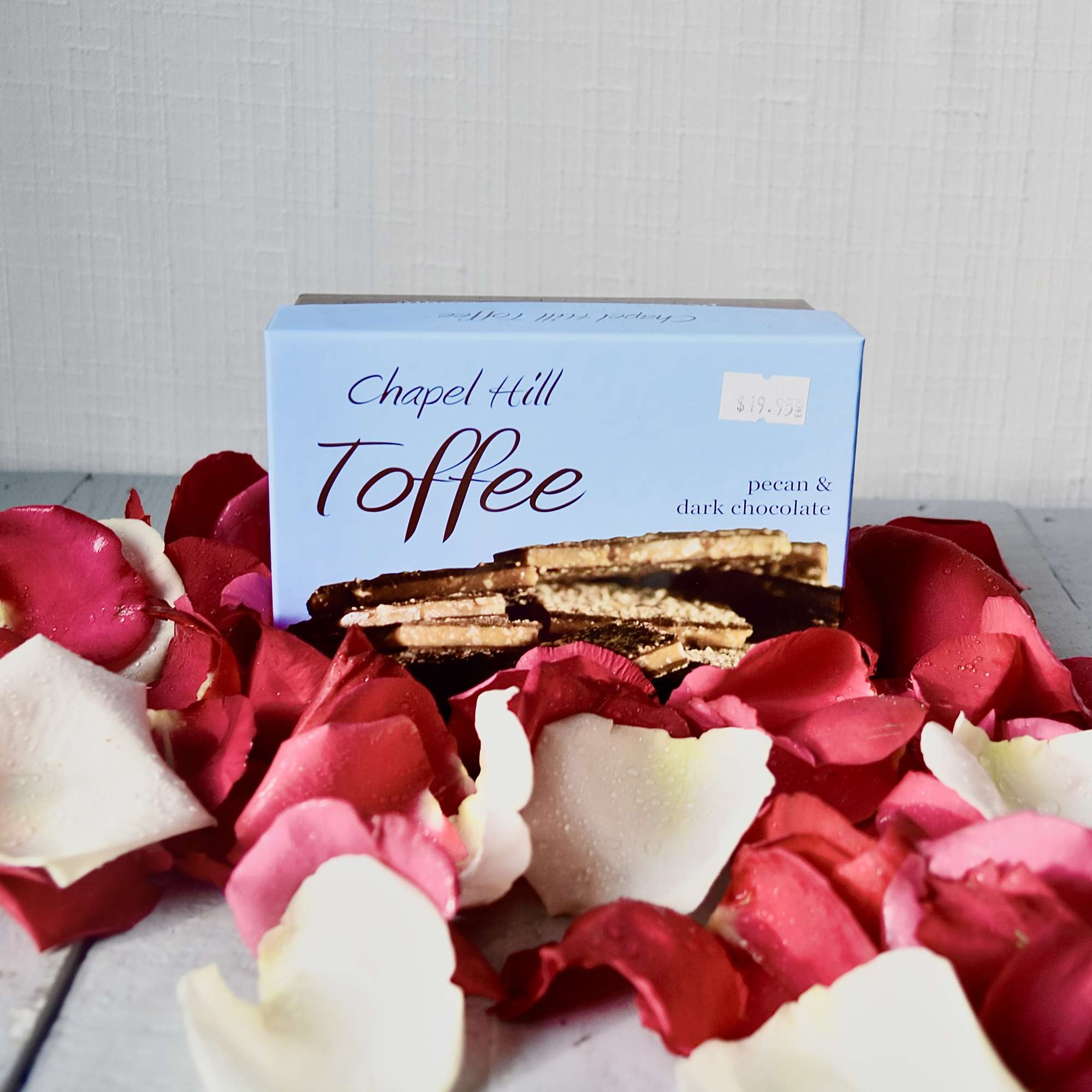 Box of toffee surrounded by red and white rose petals