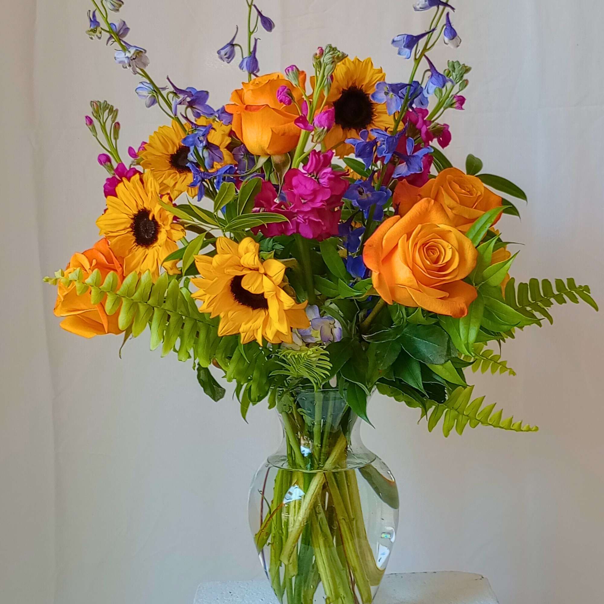 Bouquet of orange roses, sunflowers, and blue flowers in a glass vase