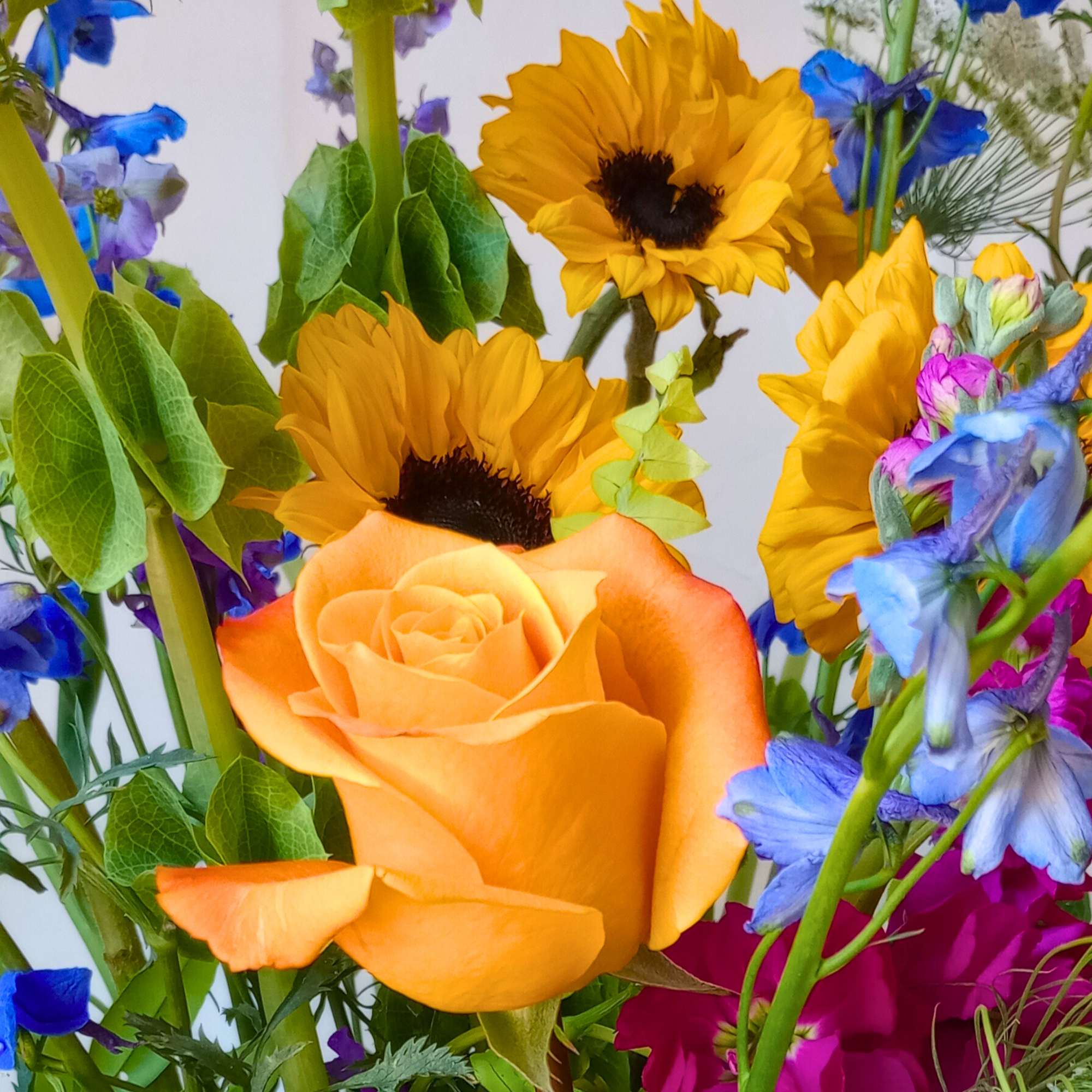 Orange rose with yellow sunflowers and blue flowers in a mixed bouquet