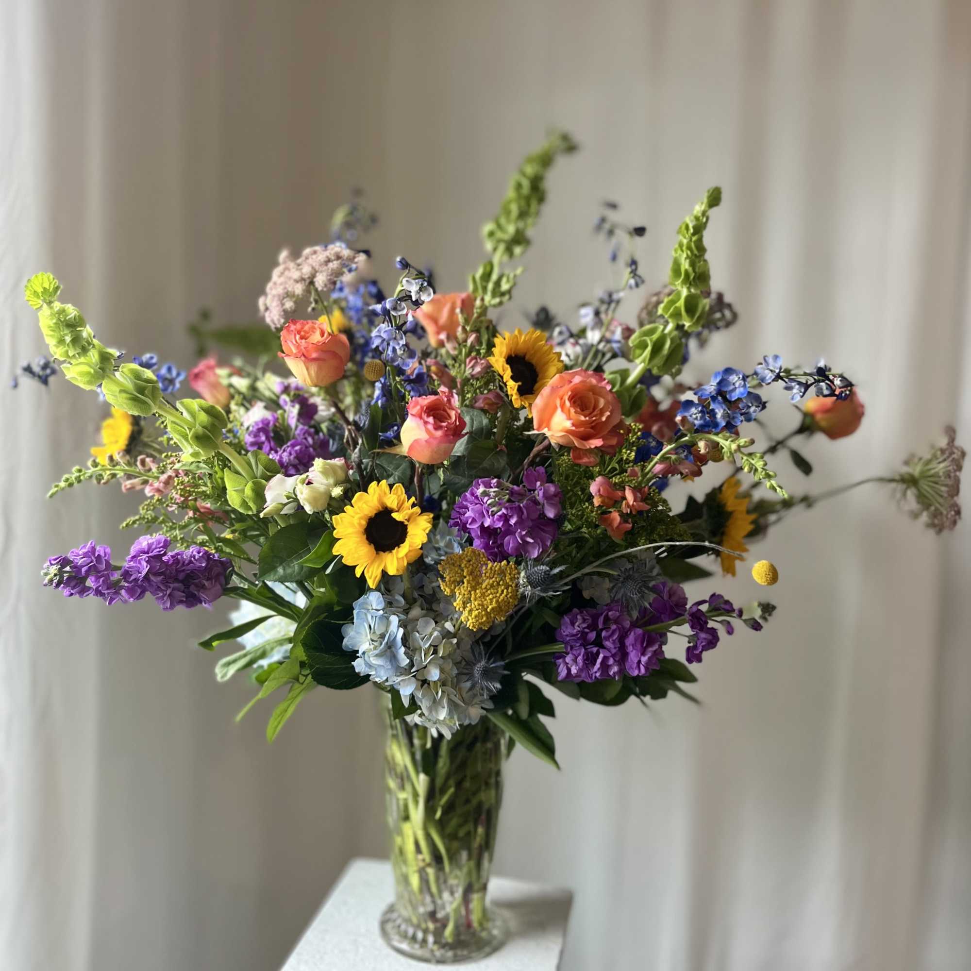 Mixed bouquet of sunflowers, roses, and purple blooms in a clear glass vase