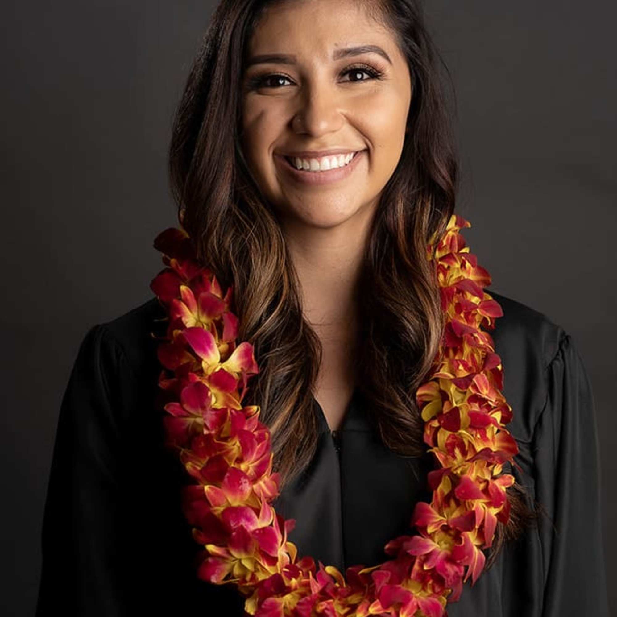 Woman wearing a red and yellow orchid lei over a black gown
