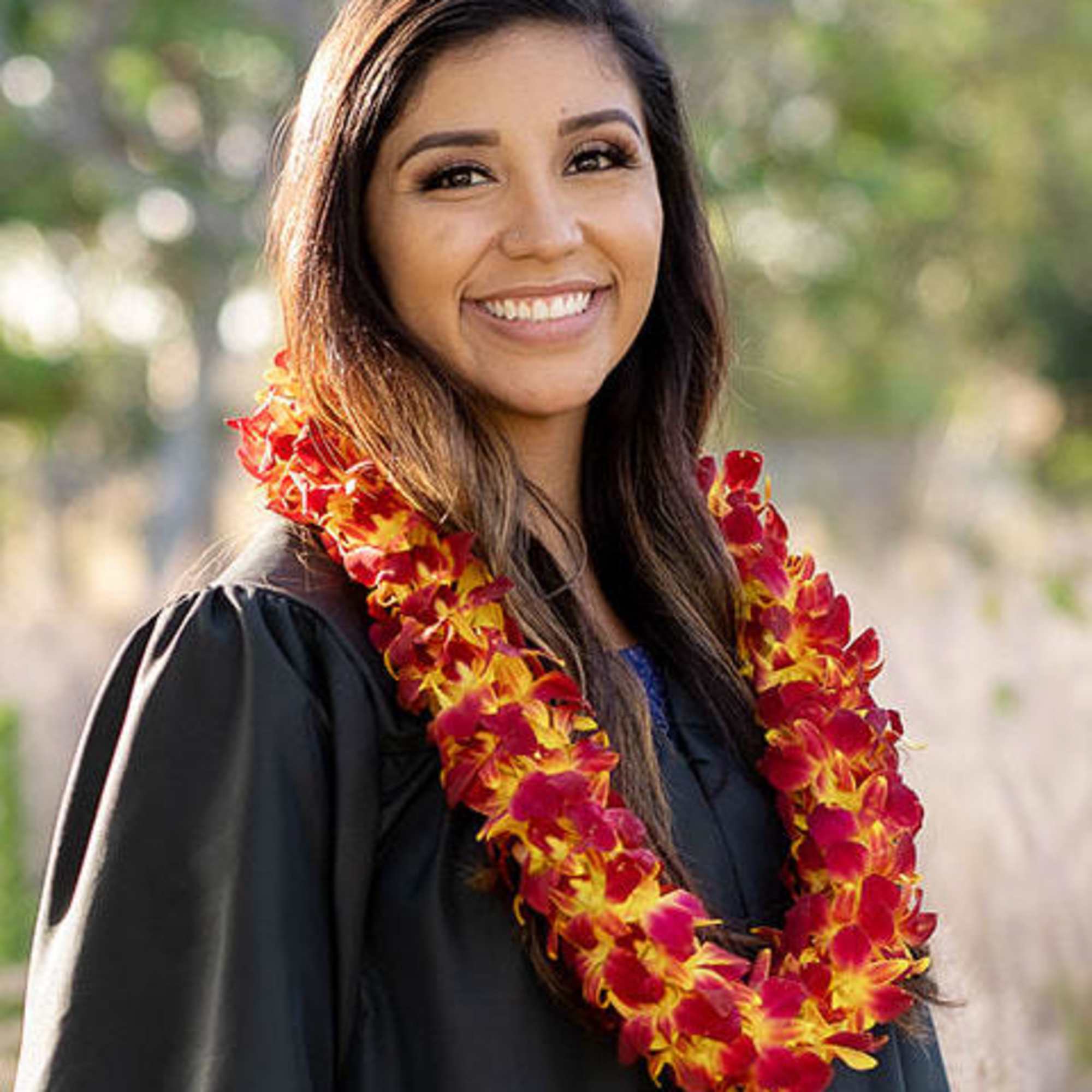 Woman in graduation gown wearing a red and yellow flower lei