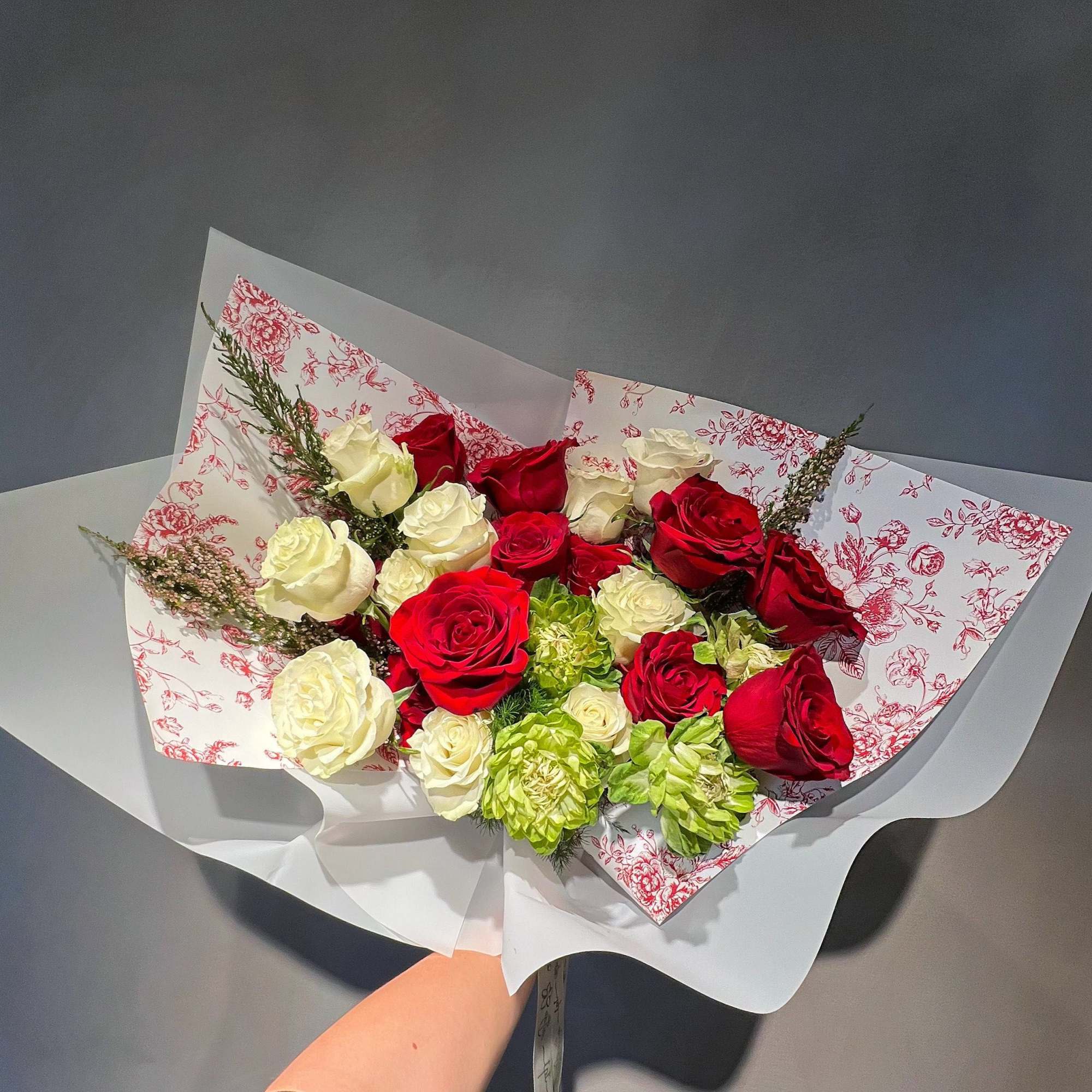Bouquet of red and white roses with green blooms in patterned wrapping