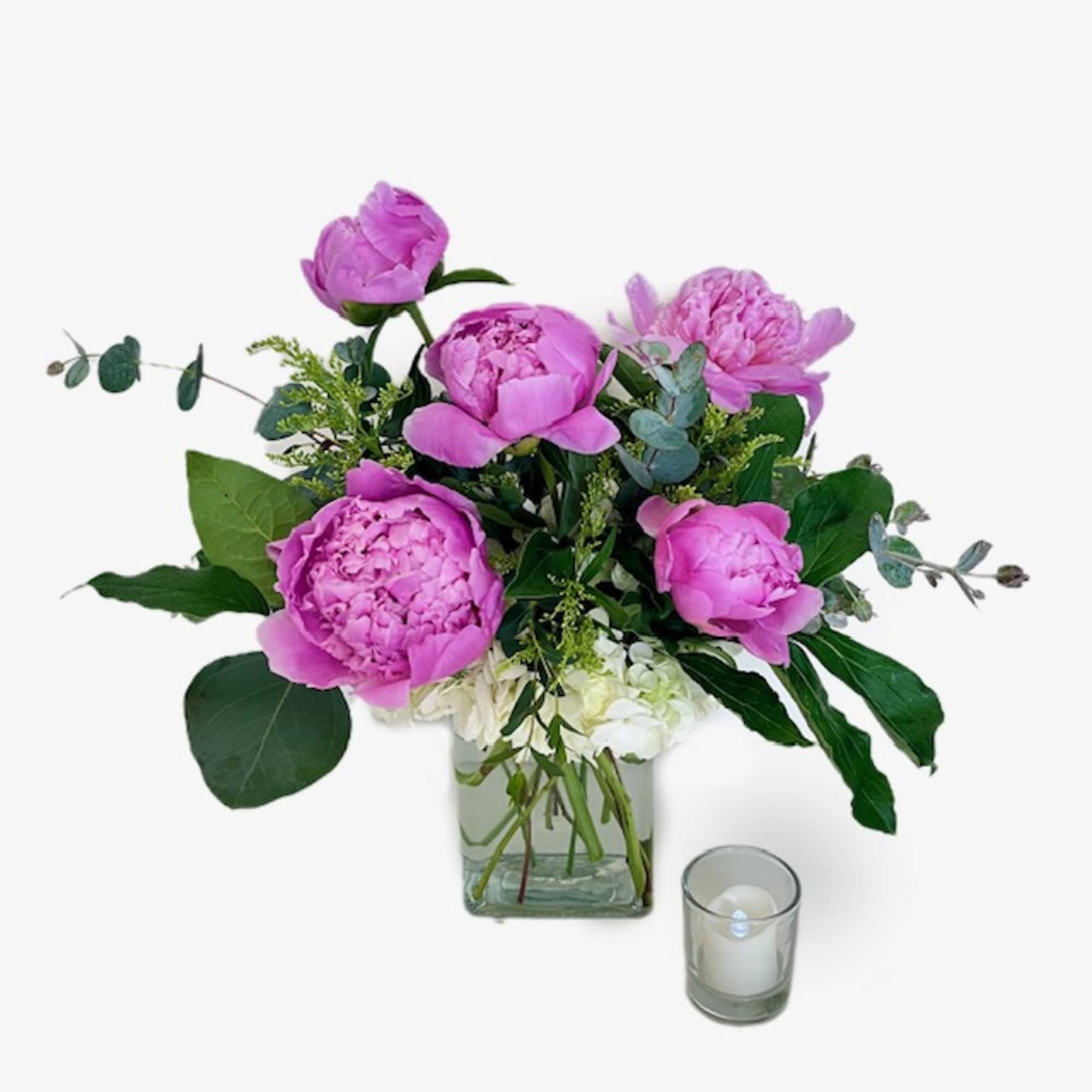 Pink peonies in a glass vase with a small candle beside it