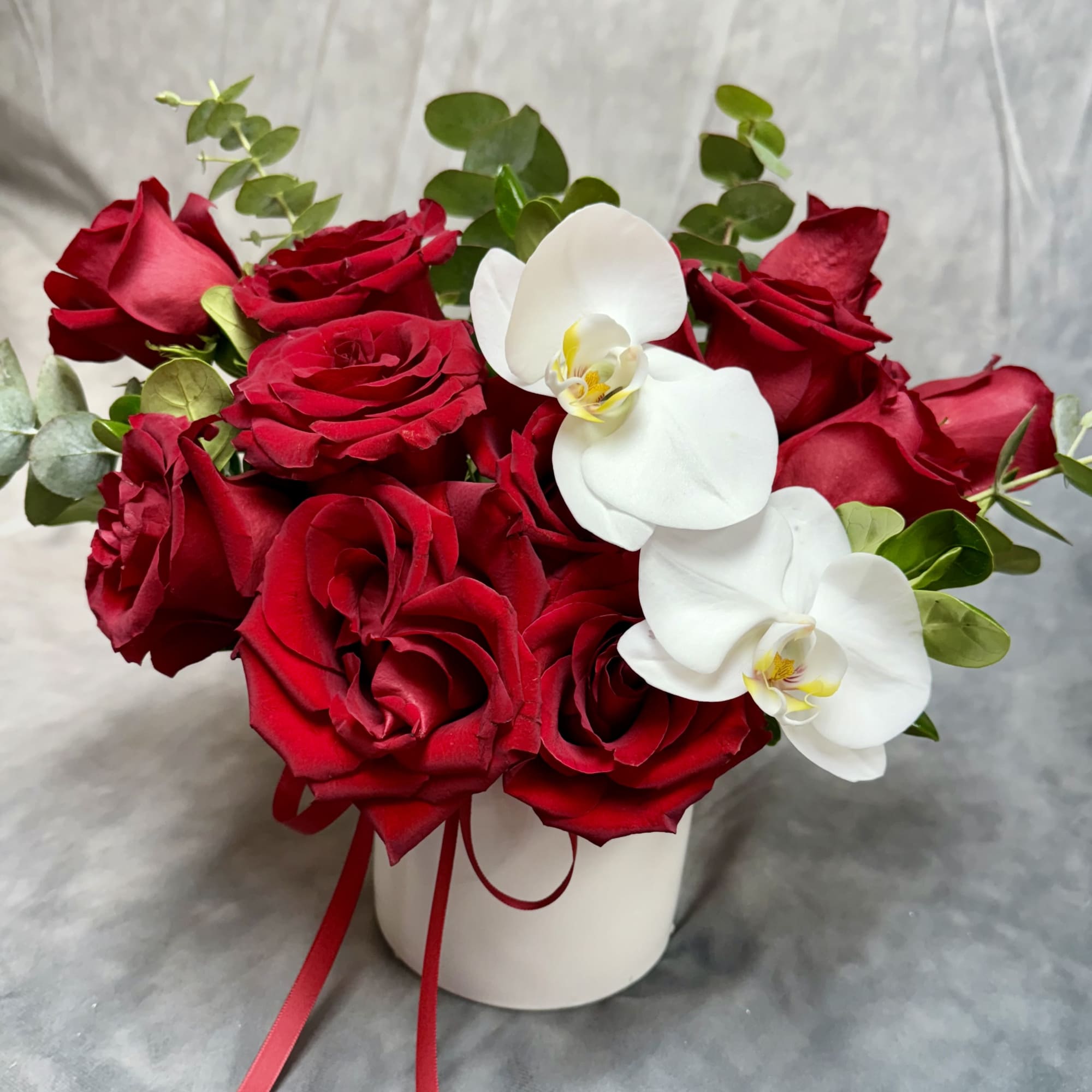Red roses and white orchids arranged in a white vase