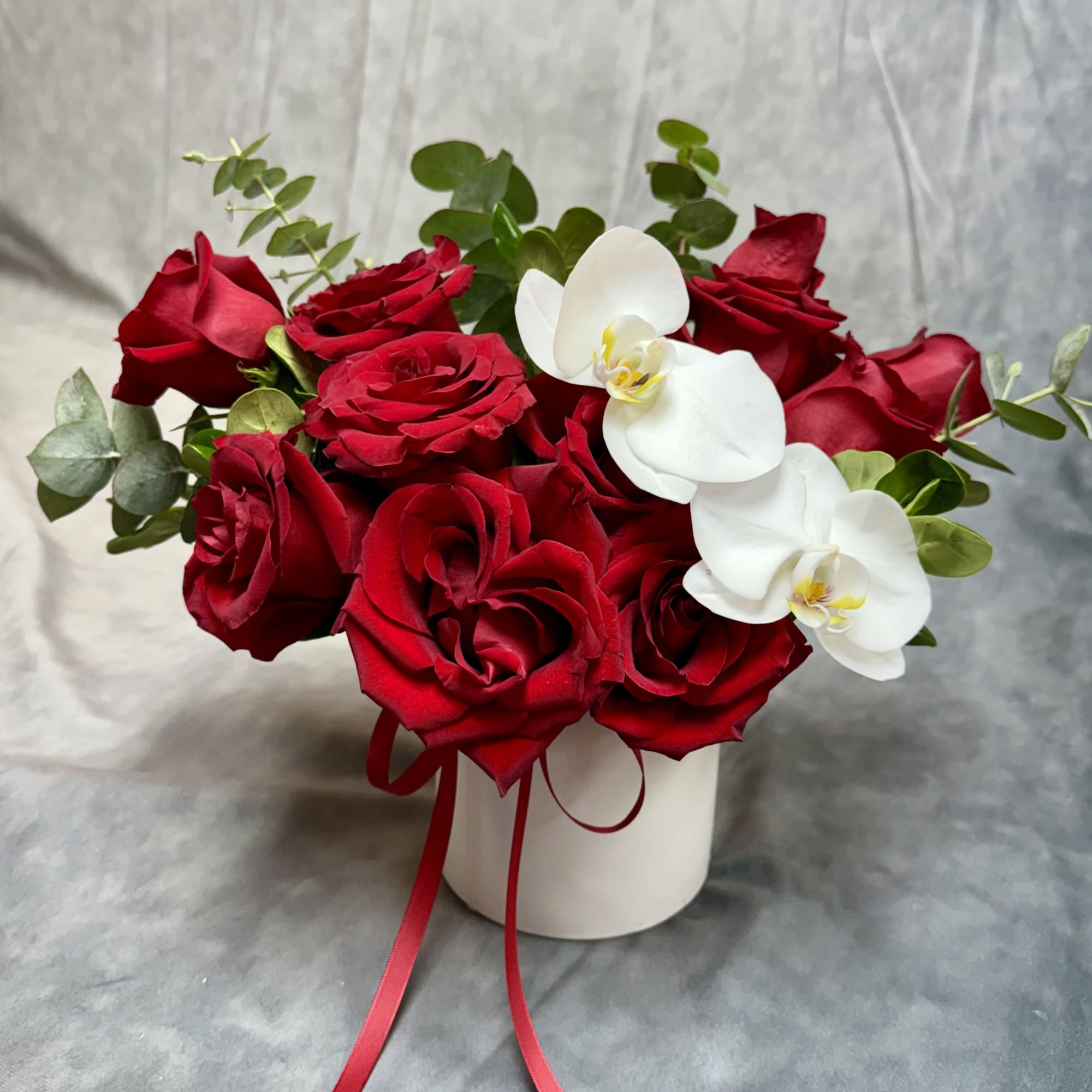 Red roses and white orchids in a white vase with a red ribbon