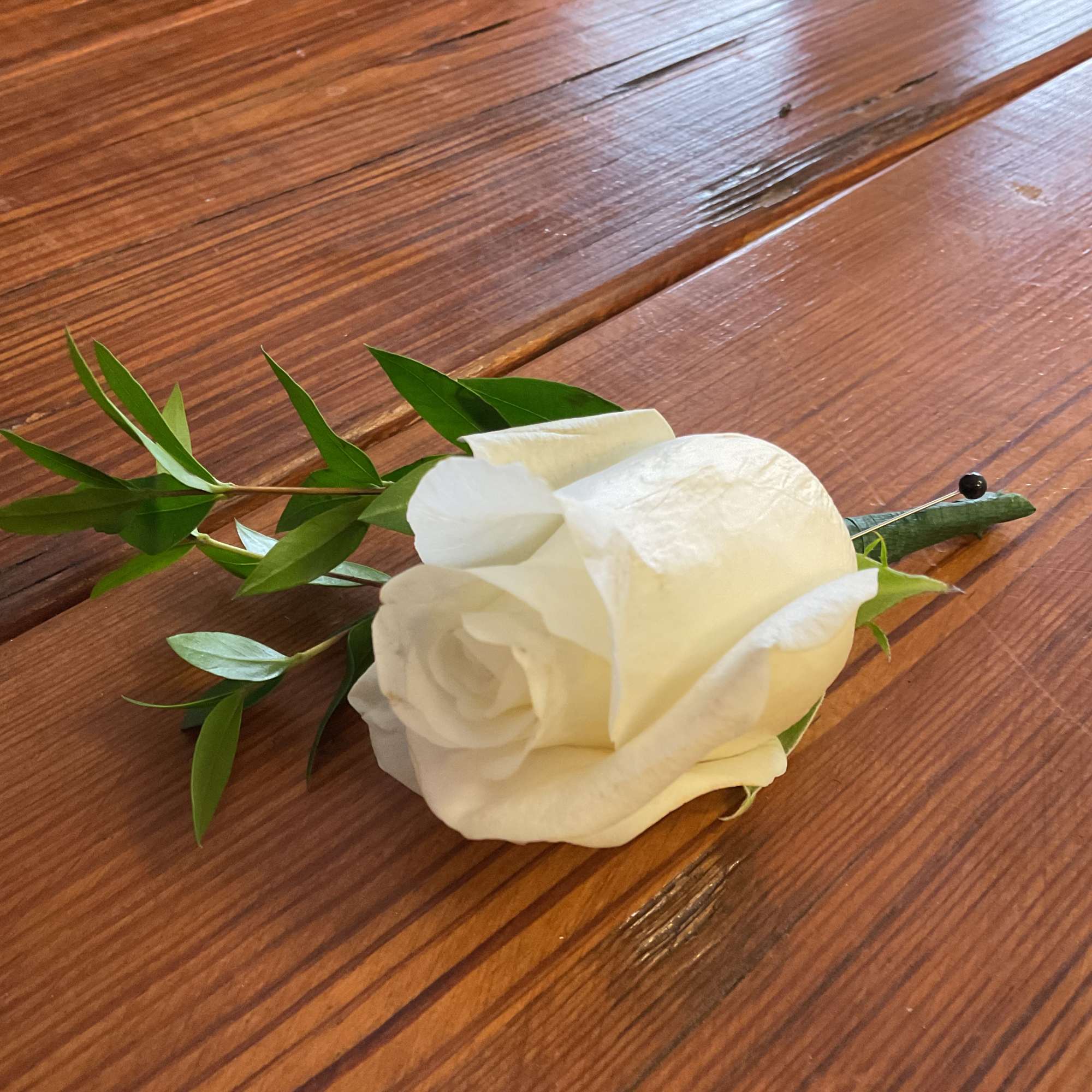 Single white rose boutonniere with pin on a wooden surface