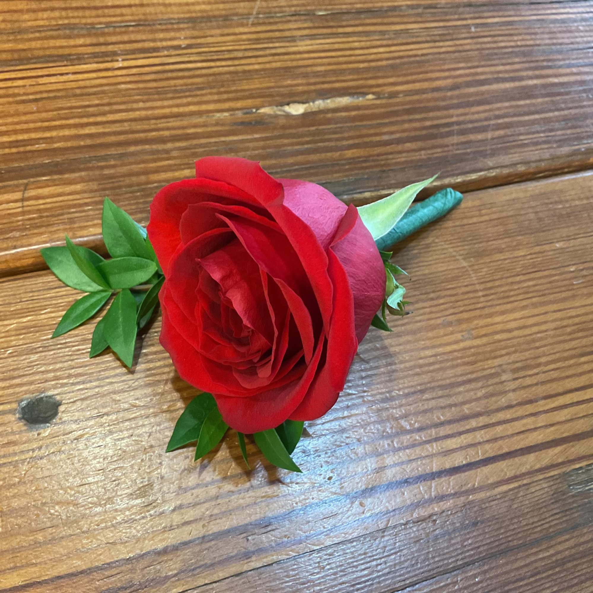 Single red rose boutonniere with wrapped stem on a wooden surface
