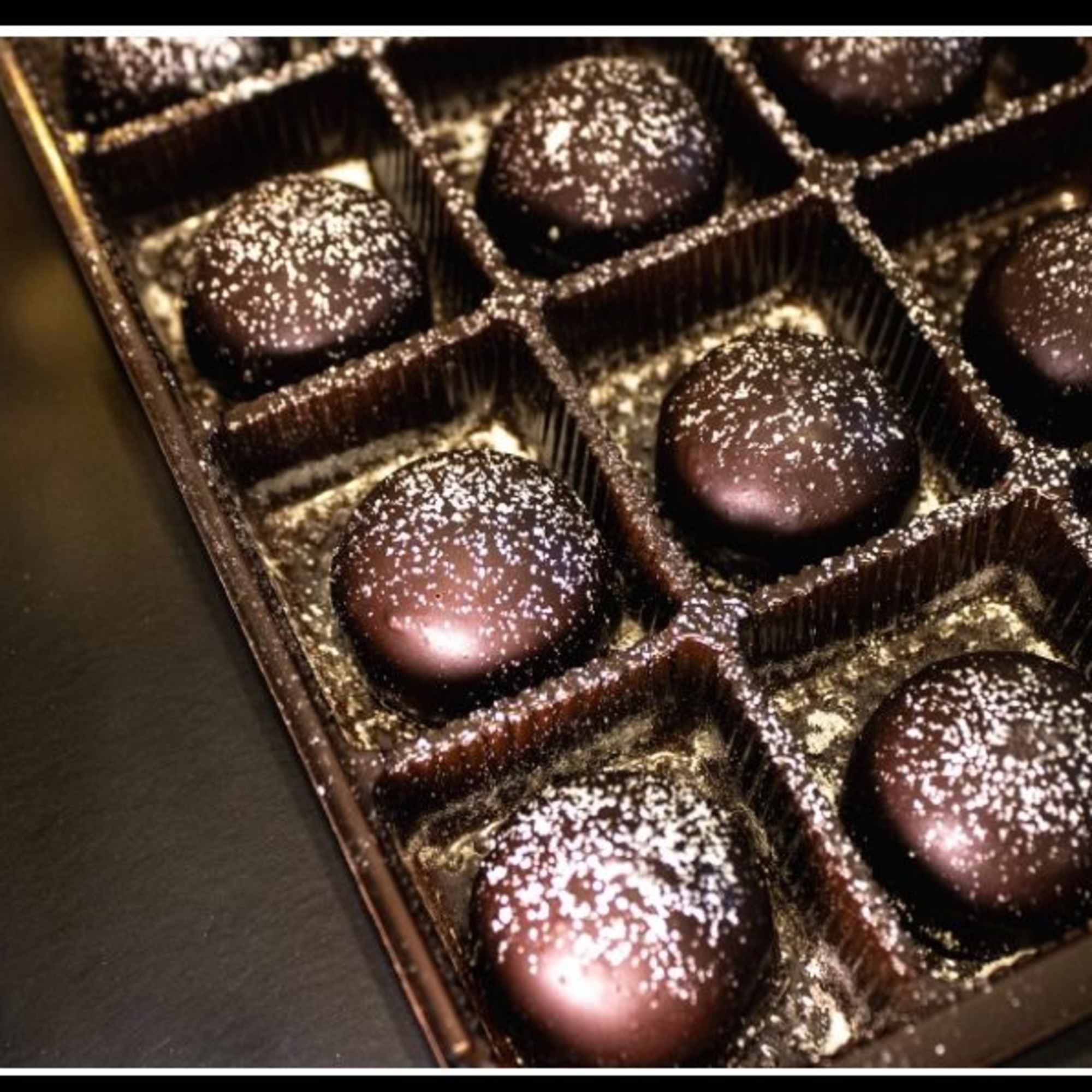 Box of round dark chocolates dusted with white sprinkles in a plastic tray