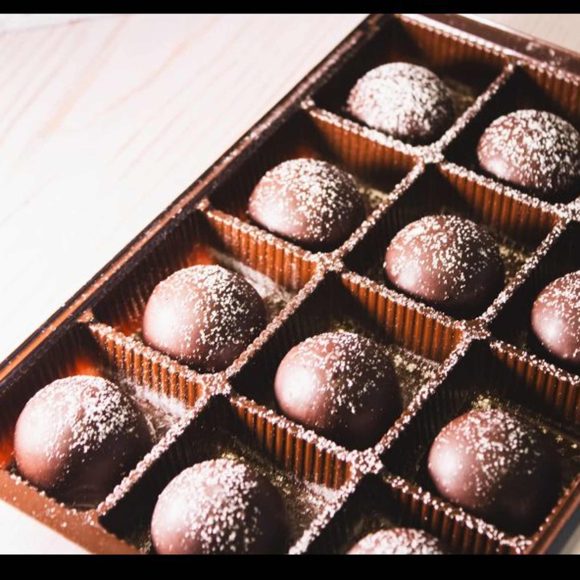 Box of round chocolate truffles in a plastic tray, each dusted with powdered sugar