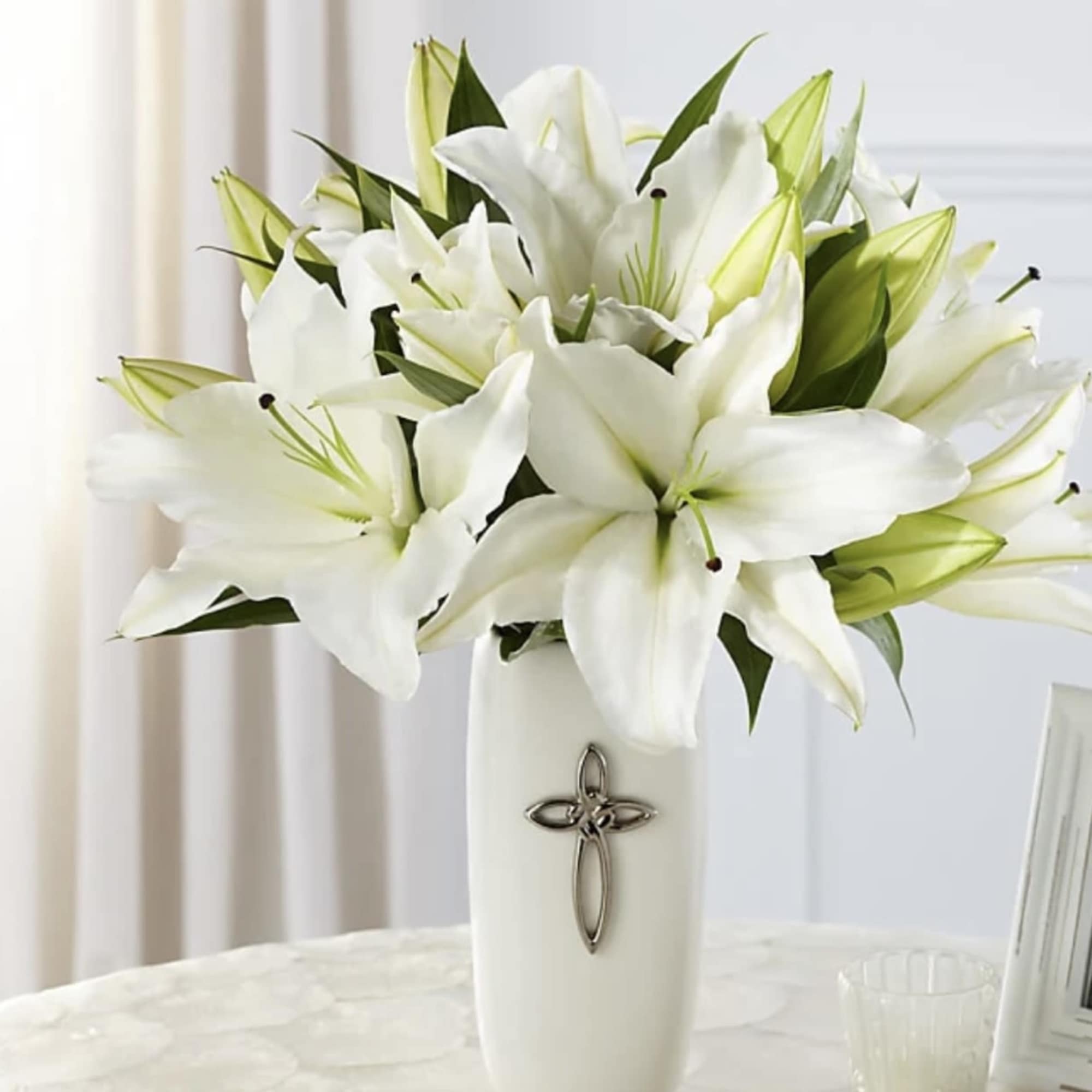 White lilies arranged in a tall white vase with a cross emblem