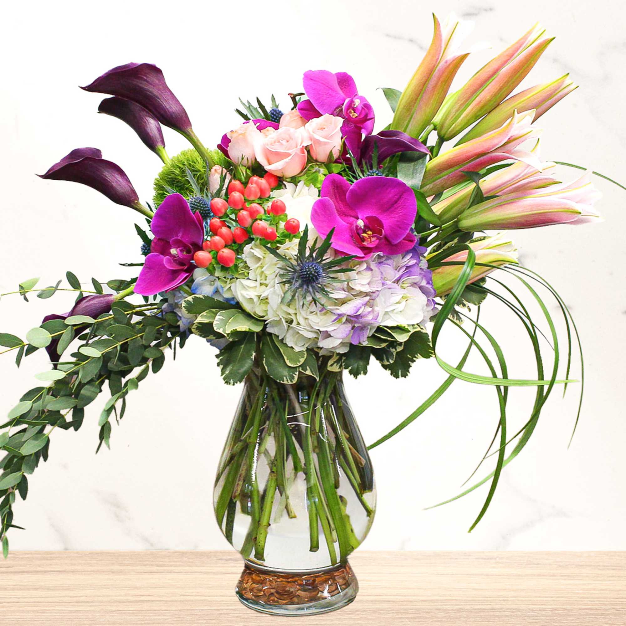Mixed bouquet with purple orchids, pink roses, lilies, and hydrangea in a glass vase