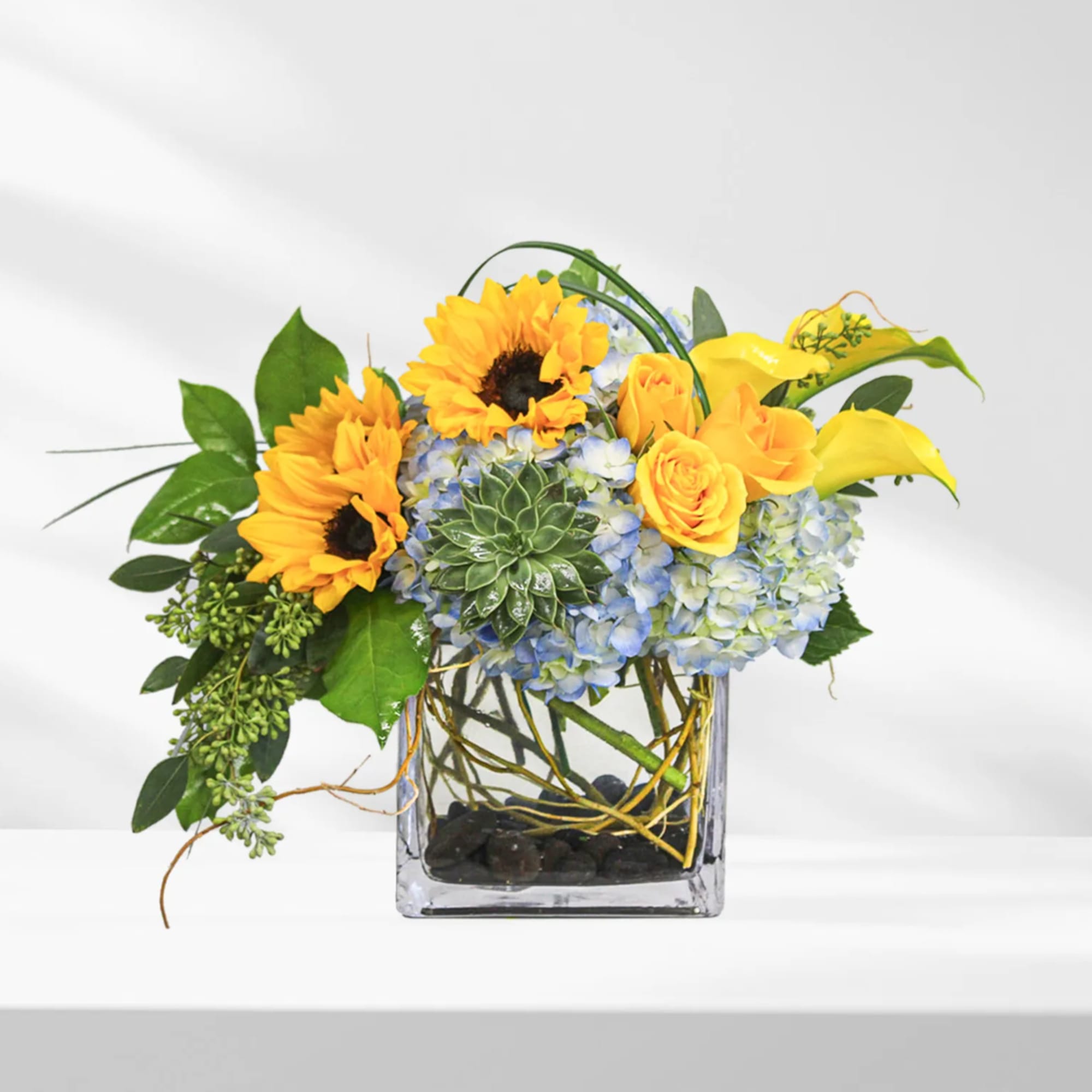 Sunflowers and yellow calla lilies in a glass cube vase with blue hydrangeas