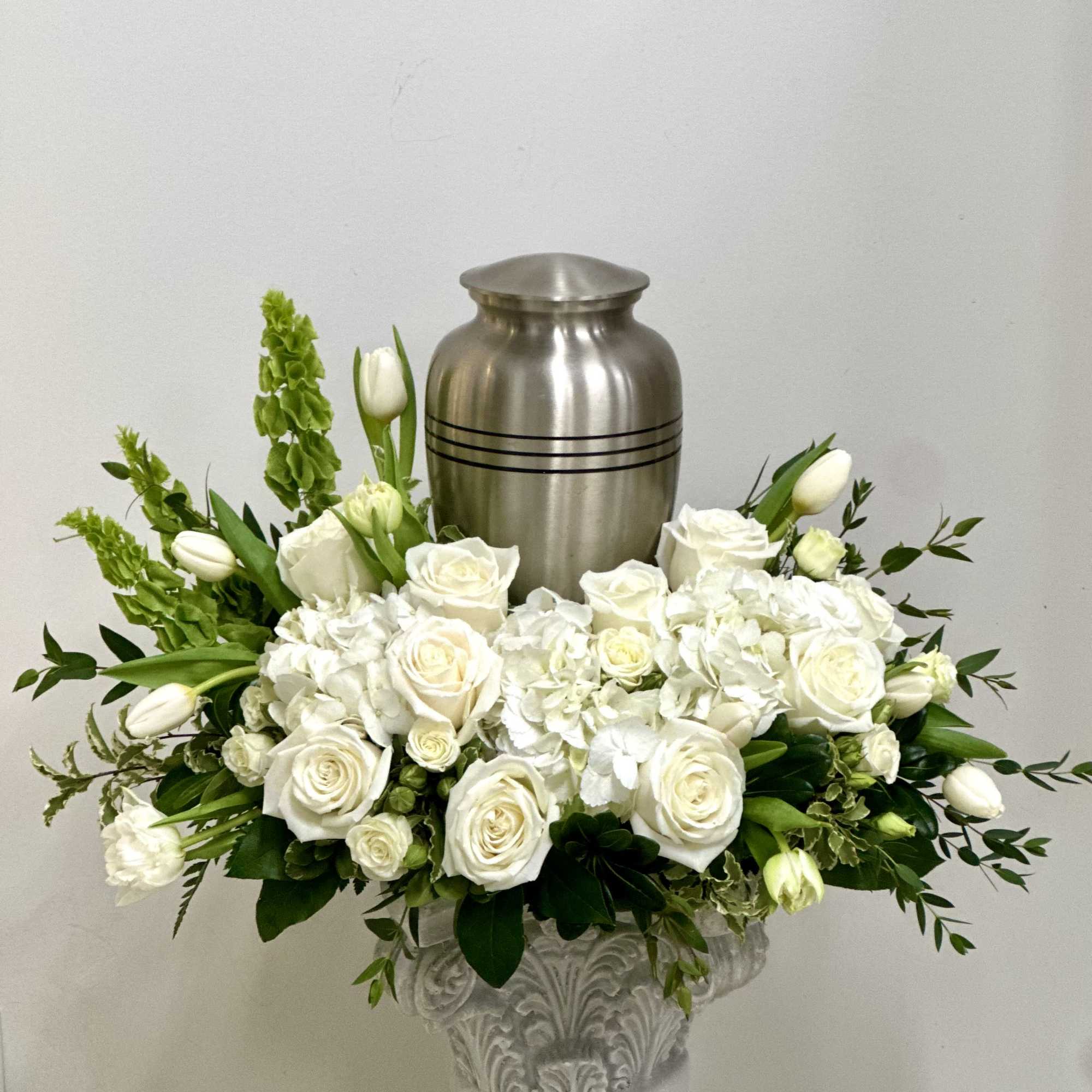 White rose and tulip arrangement in a decorative urn with a silver urn behind it