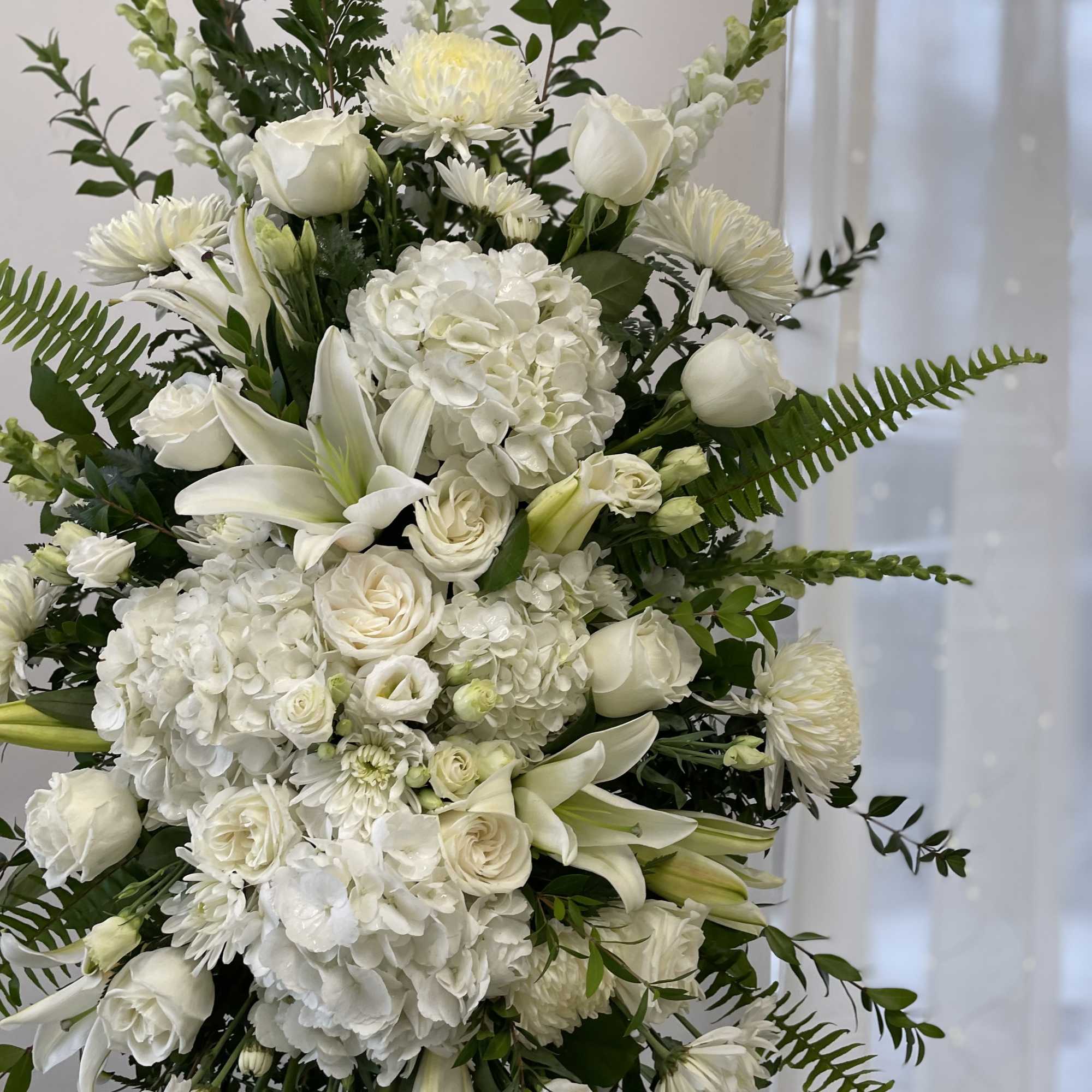 White floral arrangement with roses, lilies, hydrangeas, and chrysanthemums