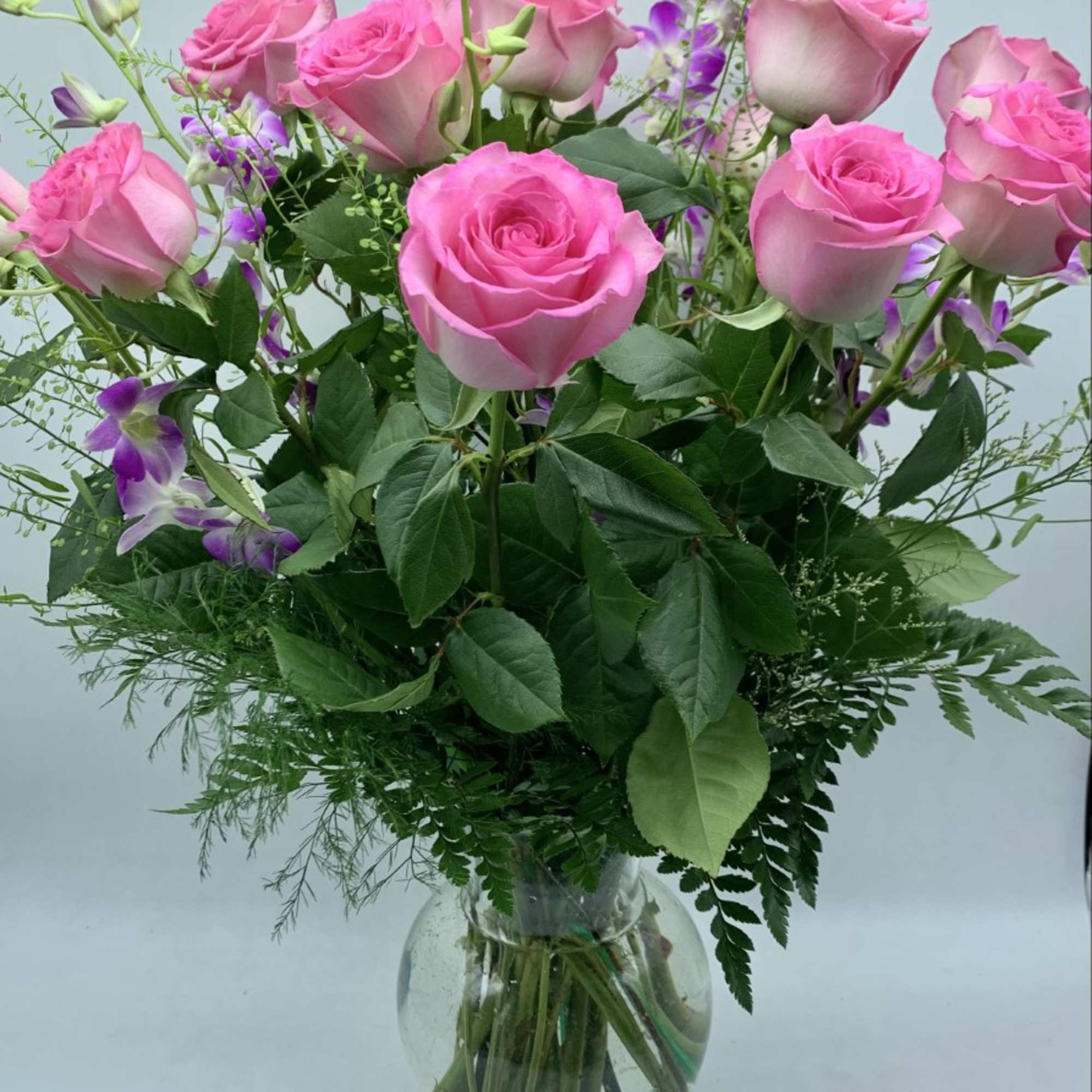 Pink roses arranged in a clear glass vase with purple accent flowers