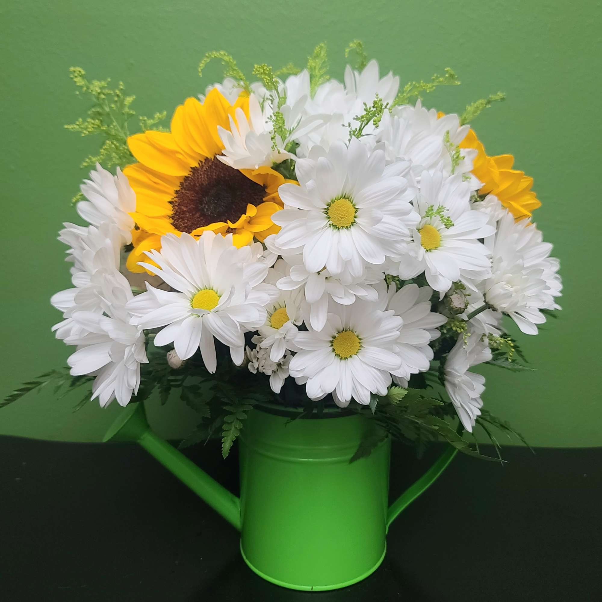 Bouquet of white daisies and yellow sunflowers in a green watering can