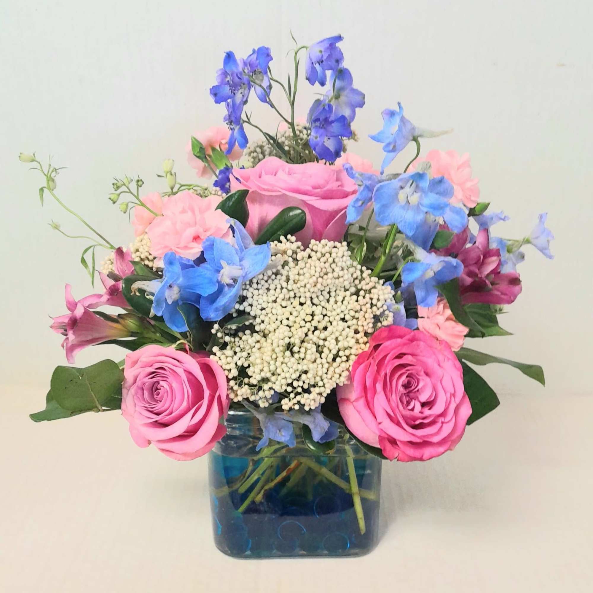 Pink roses and blue flowers arranged in a square glass vase