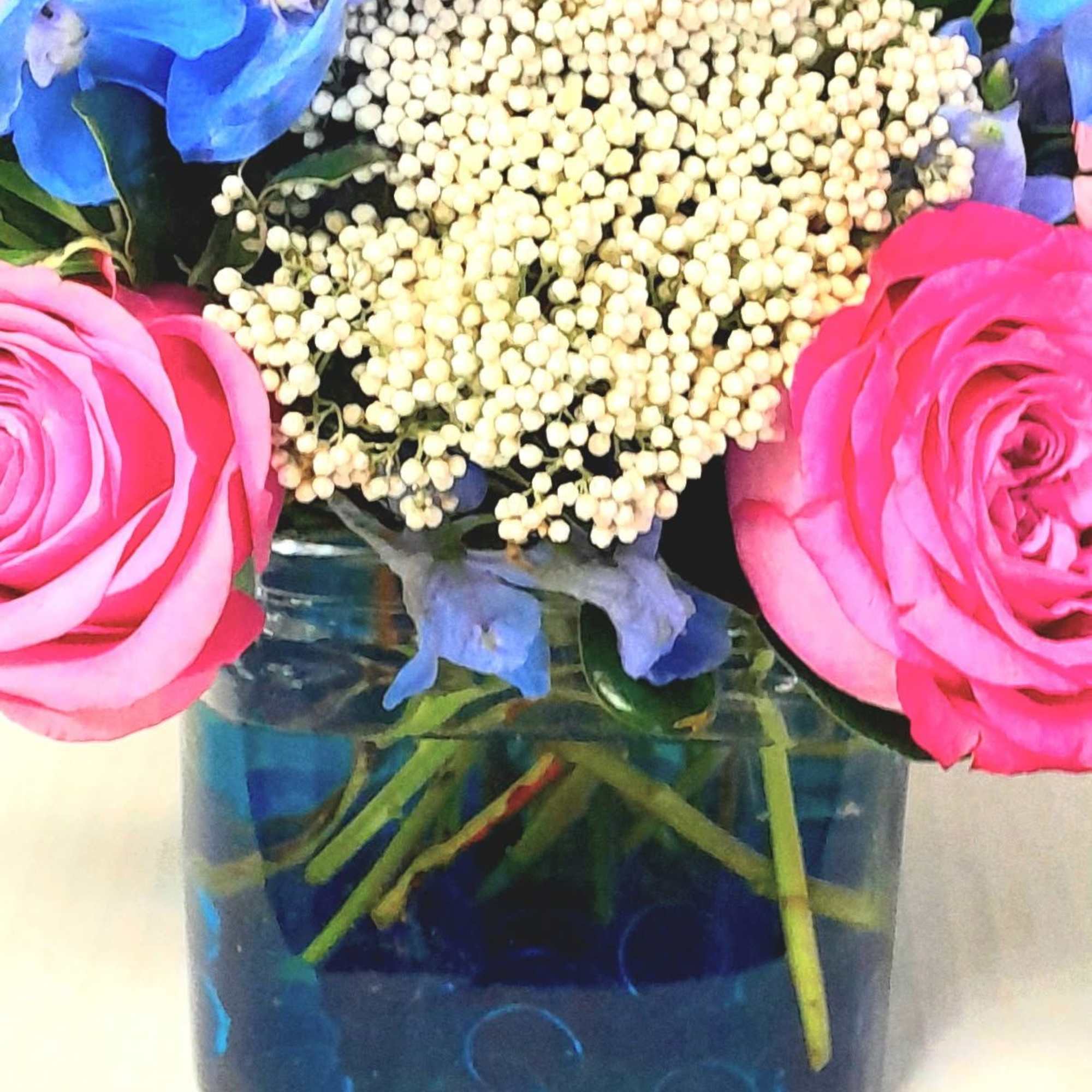 Pink roses and blue flowers in a square glass vase with white berries