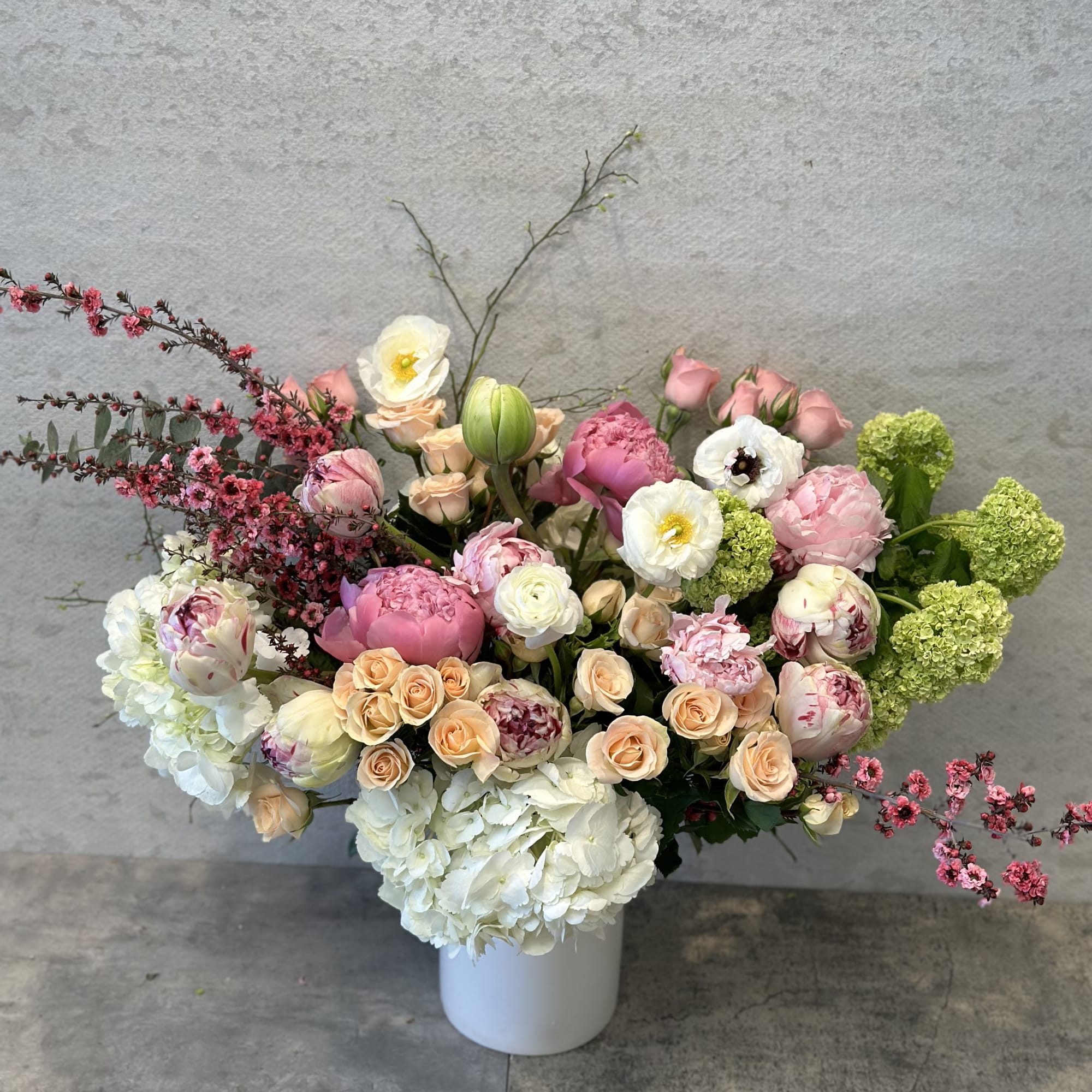 Large pastel flower arrangement in a white vase with pink, white, and peach blooms