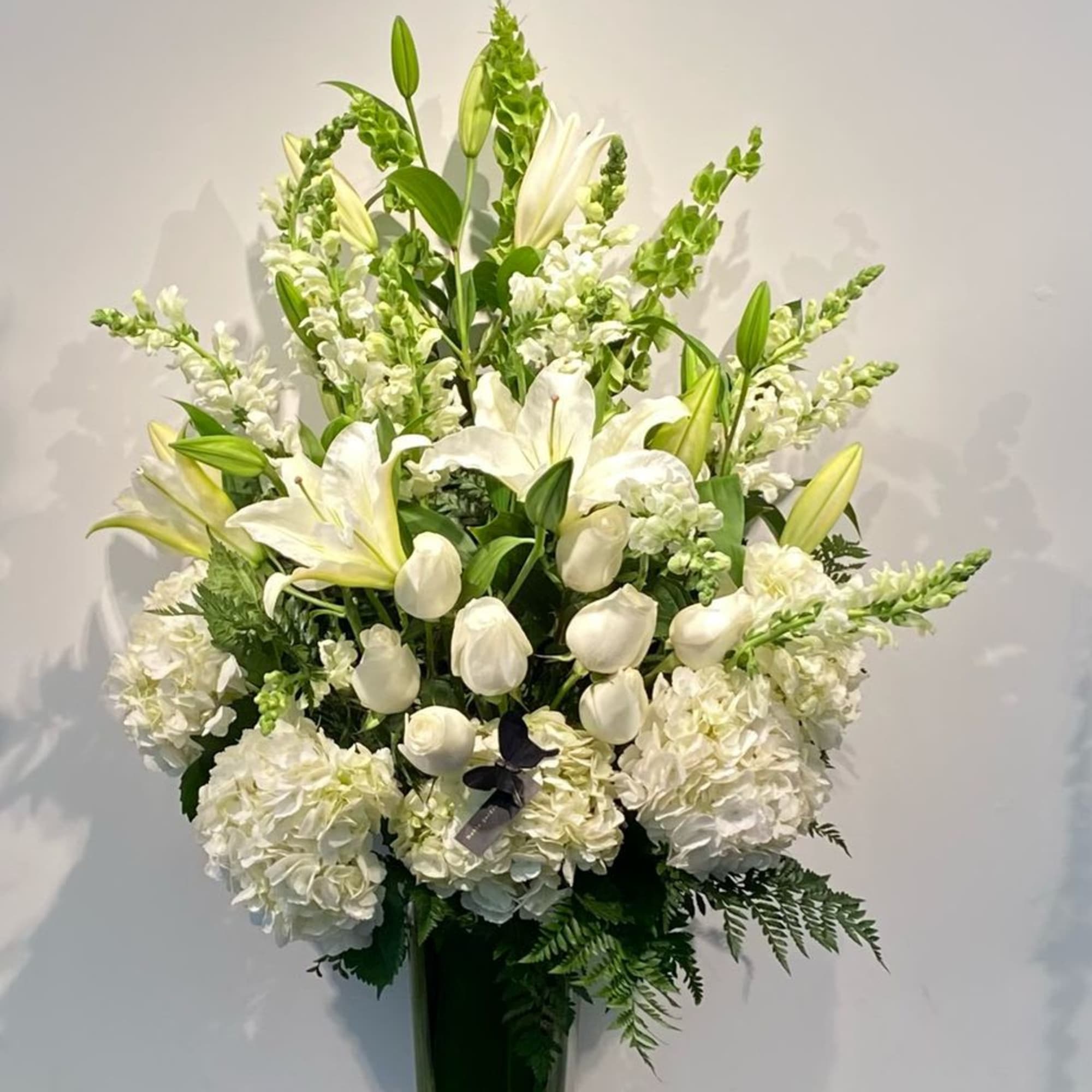 Tall white floral arrangement in a glass vase with lilies and hydrangeas