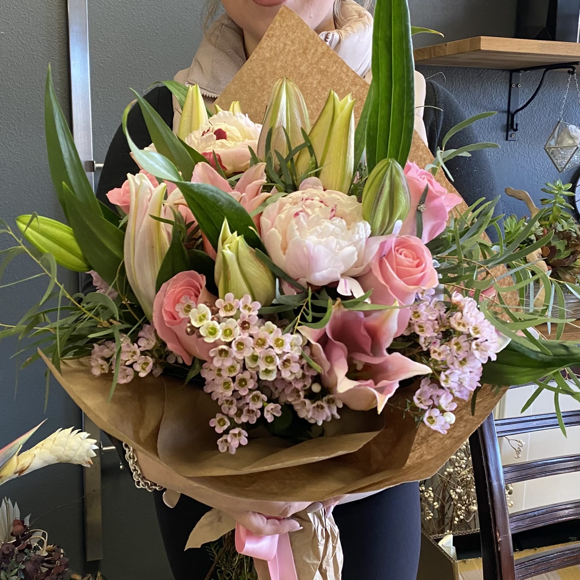 Large bouquet of pink roses, lilies, and peonies wrapped in brown paper