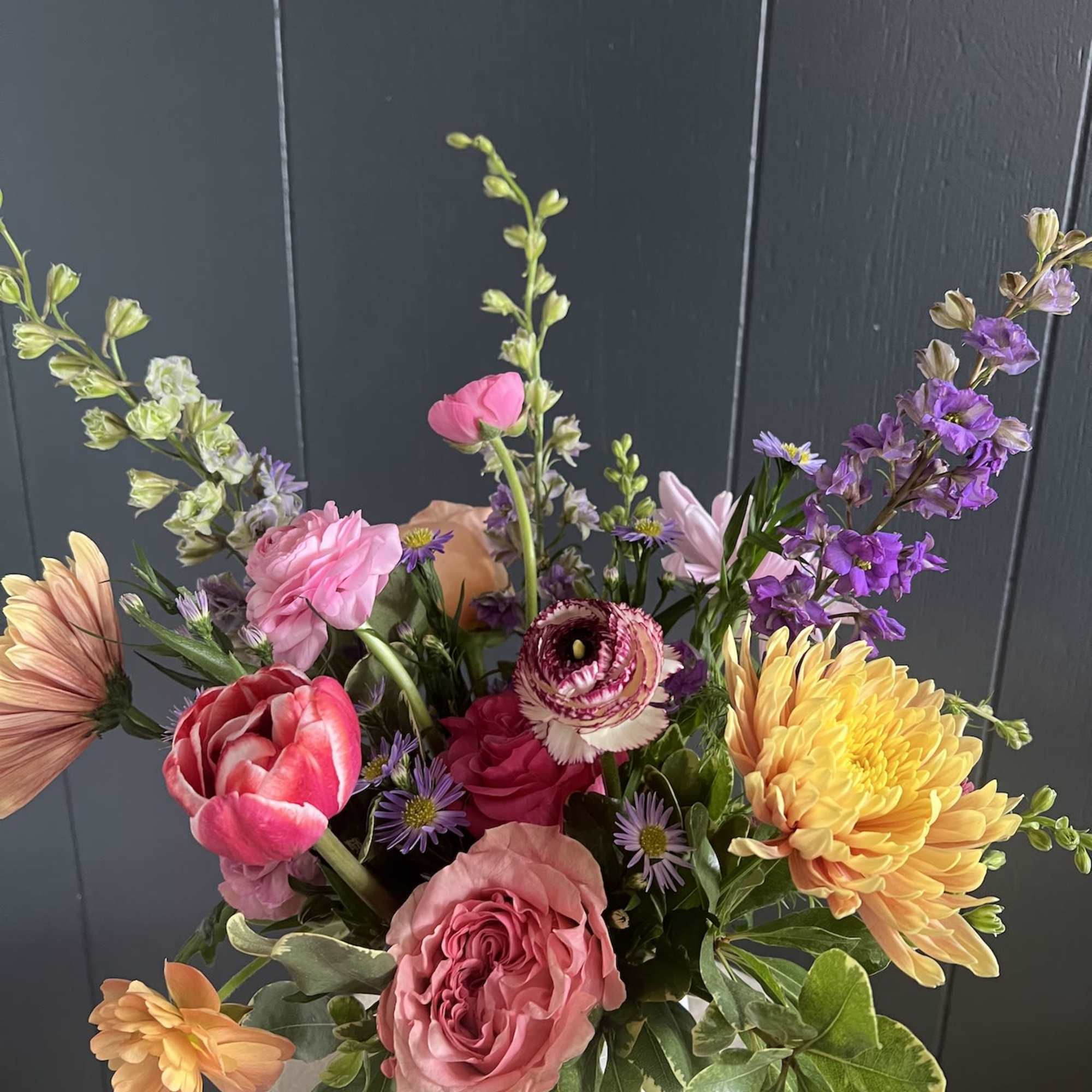 Mixed bouquet of pink, purple, yellow, and peach flowers in a white vase