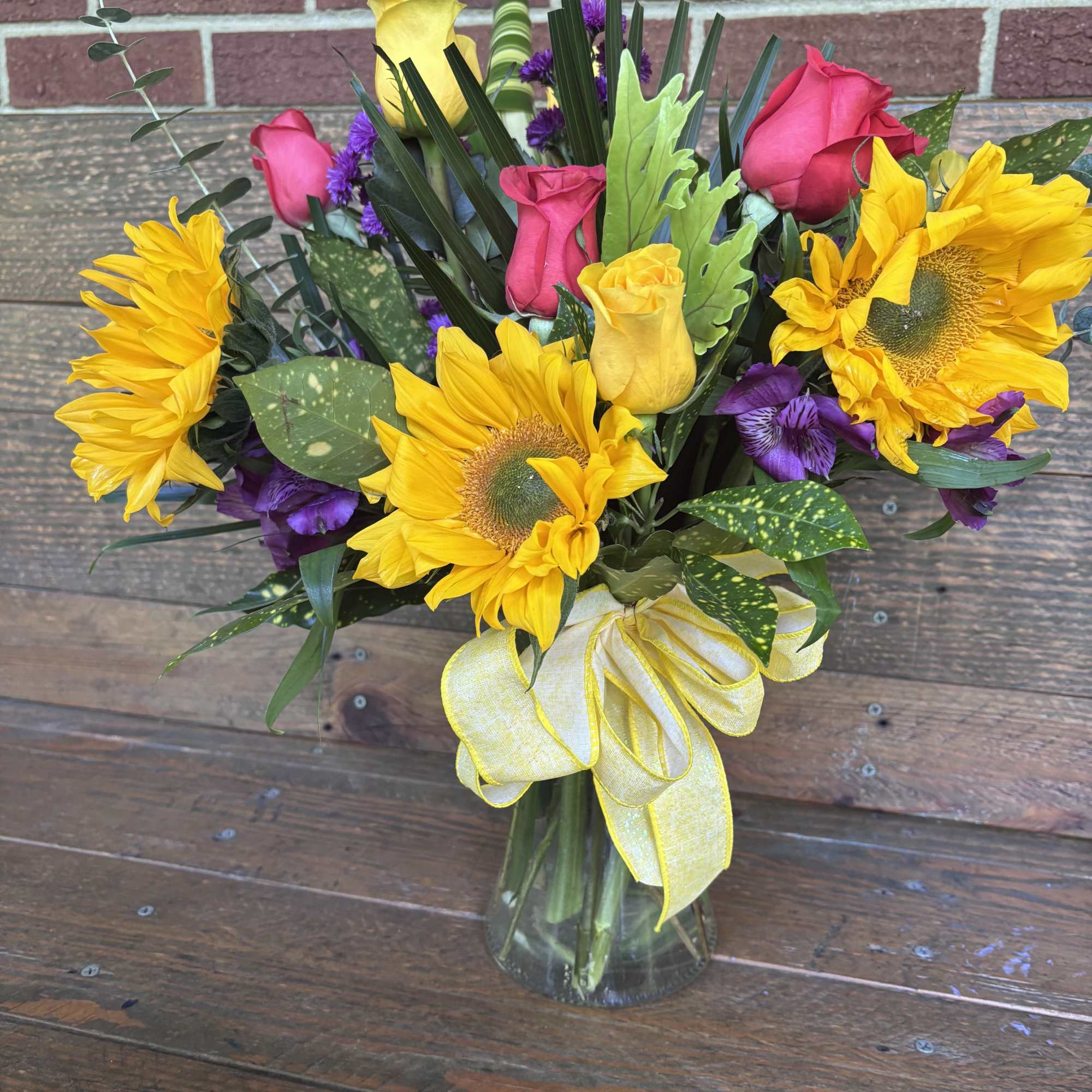 Sunflowers take center stage in this cheerful flower arrangement, paired with pink