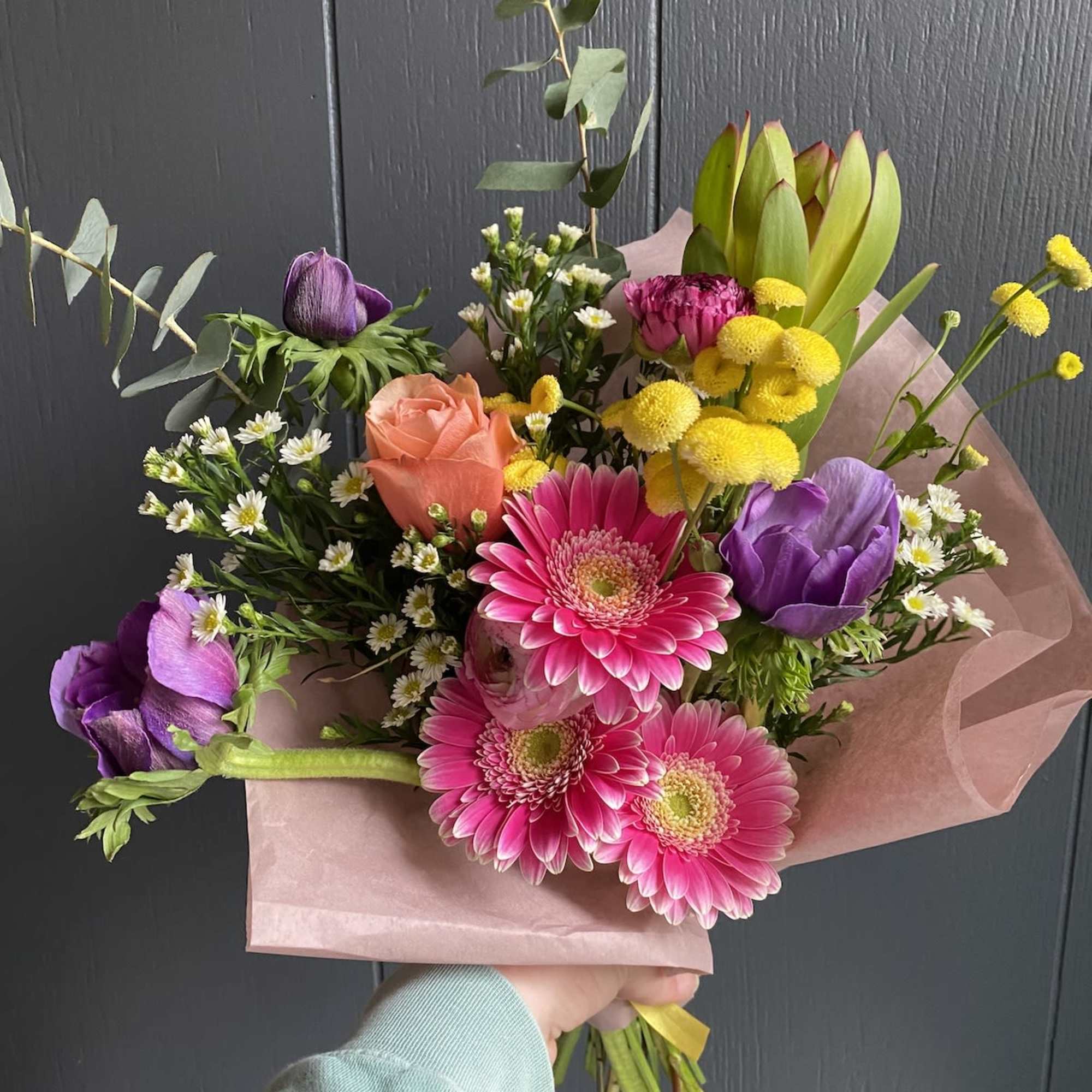 Hand-tied bouquet with pink gerberas, purple tulips, and a peach rose