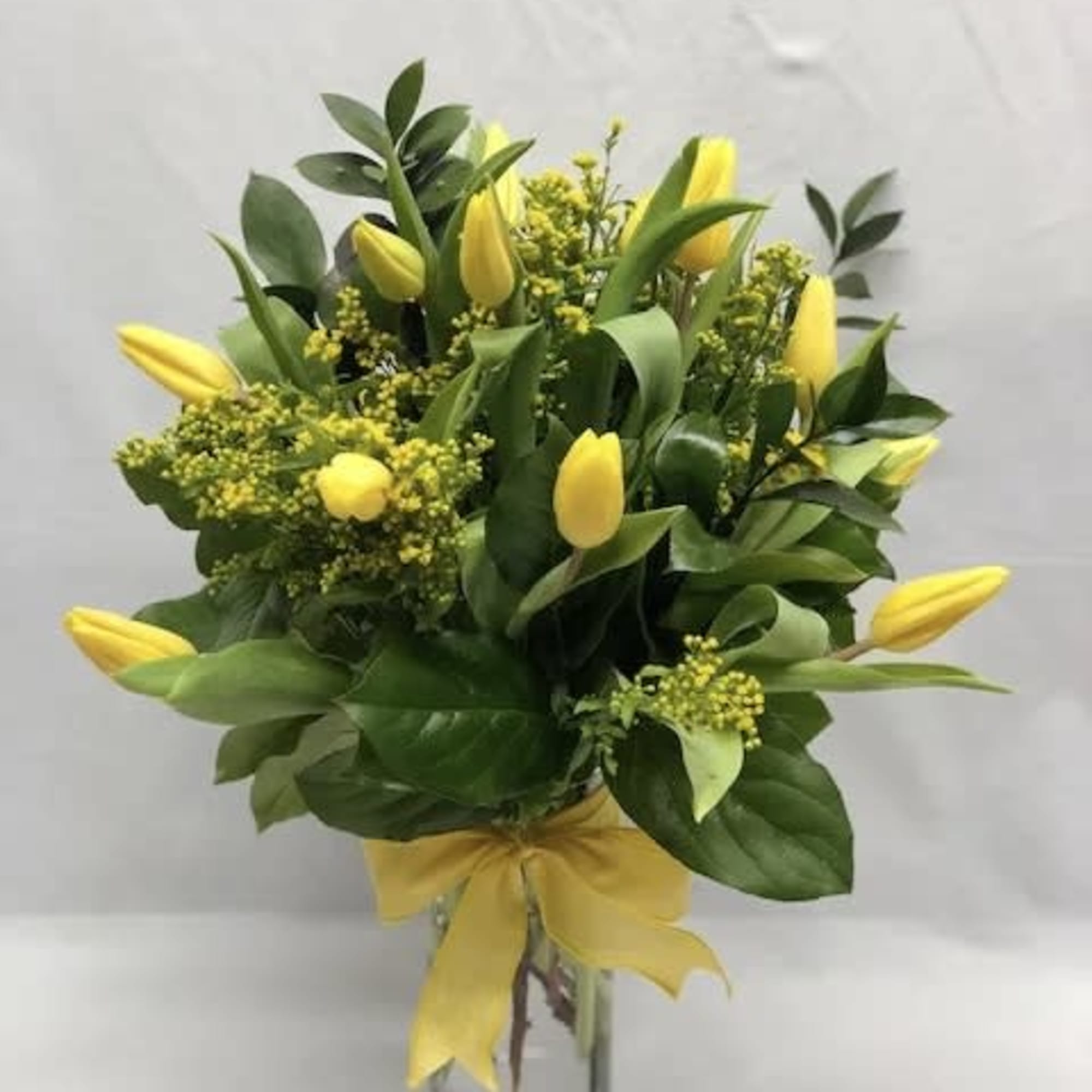 Yellow tulips arranged in a clear glass vase with a yellow ribbon