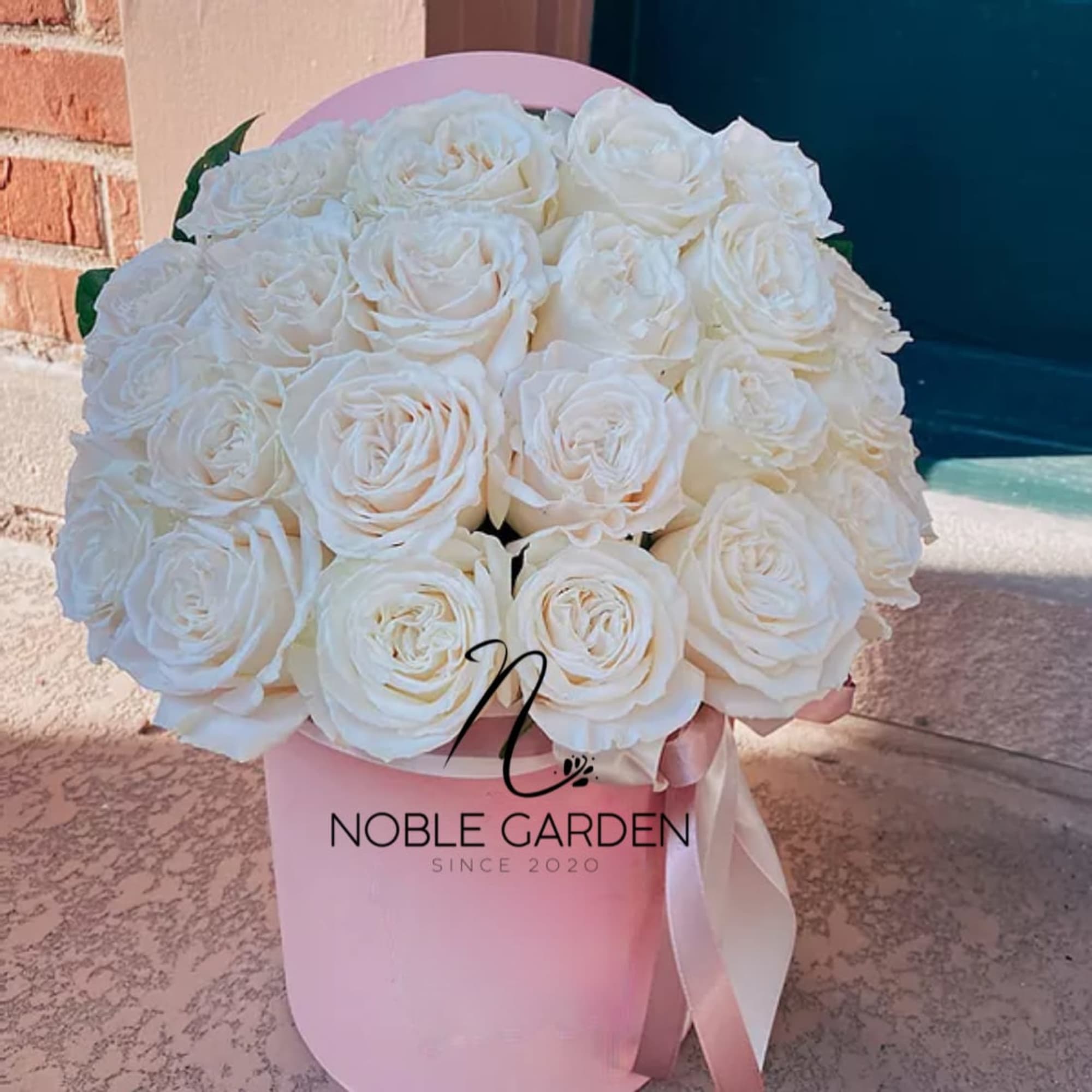 White roses arranged in a pink hat box with a ribbon.