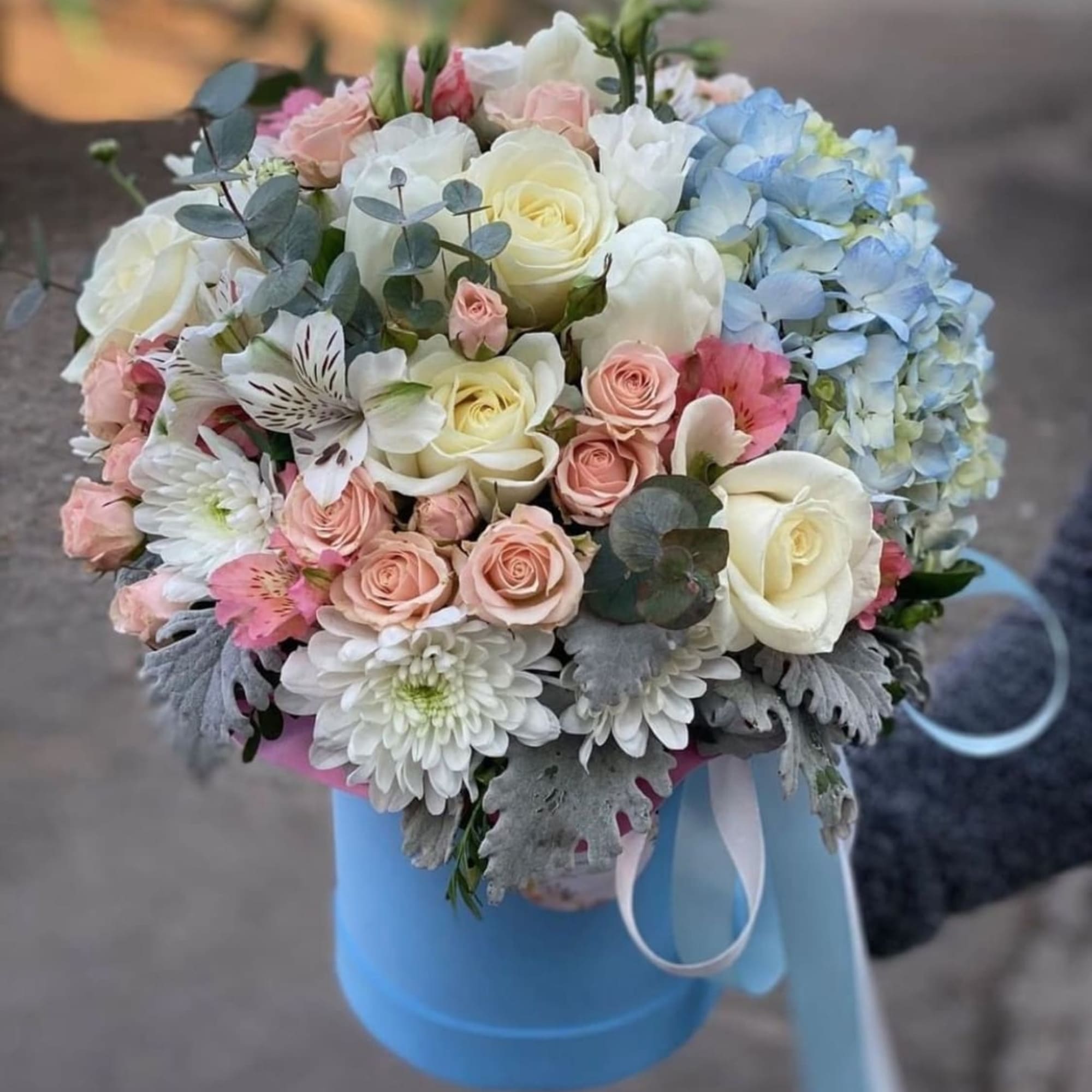 Pastel bouquet of roses, hydrangeas, and white blooms in a blue box